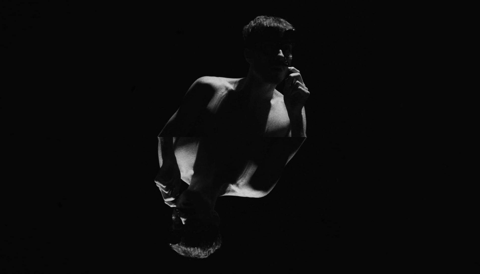 A male figure emerges frontally from the shadows. The photo is in black and white.
