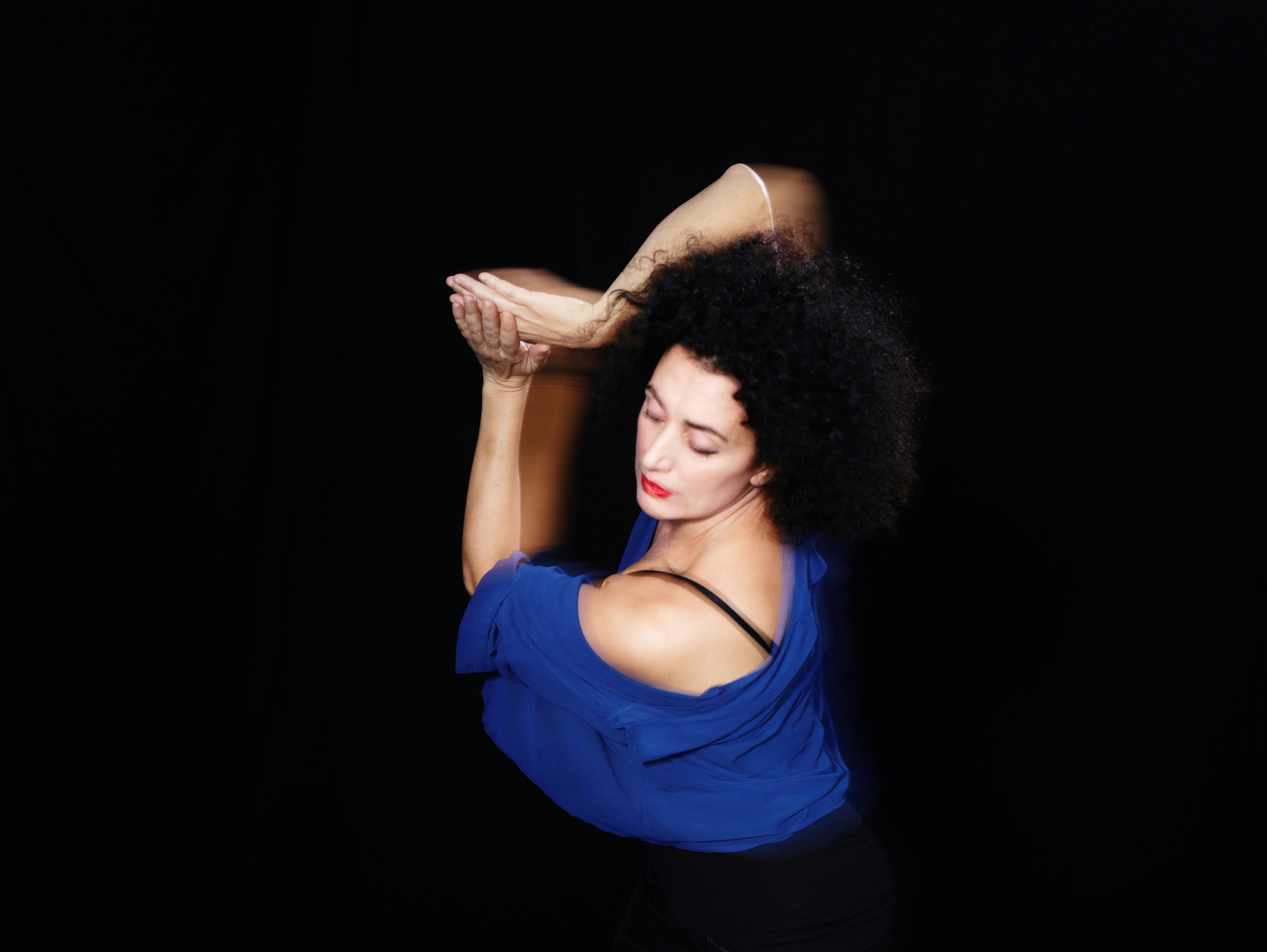 Foto su sfondo nero di Cristiana Morganti in posa di danza con le braccia unite semi alzate lateralmente