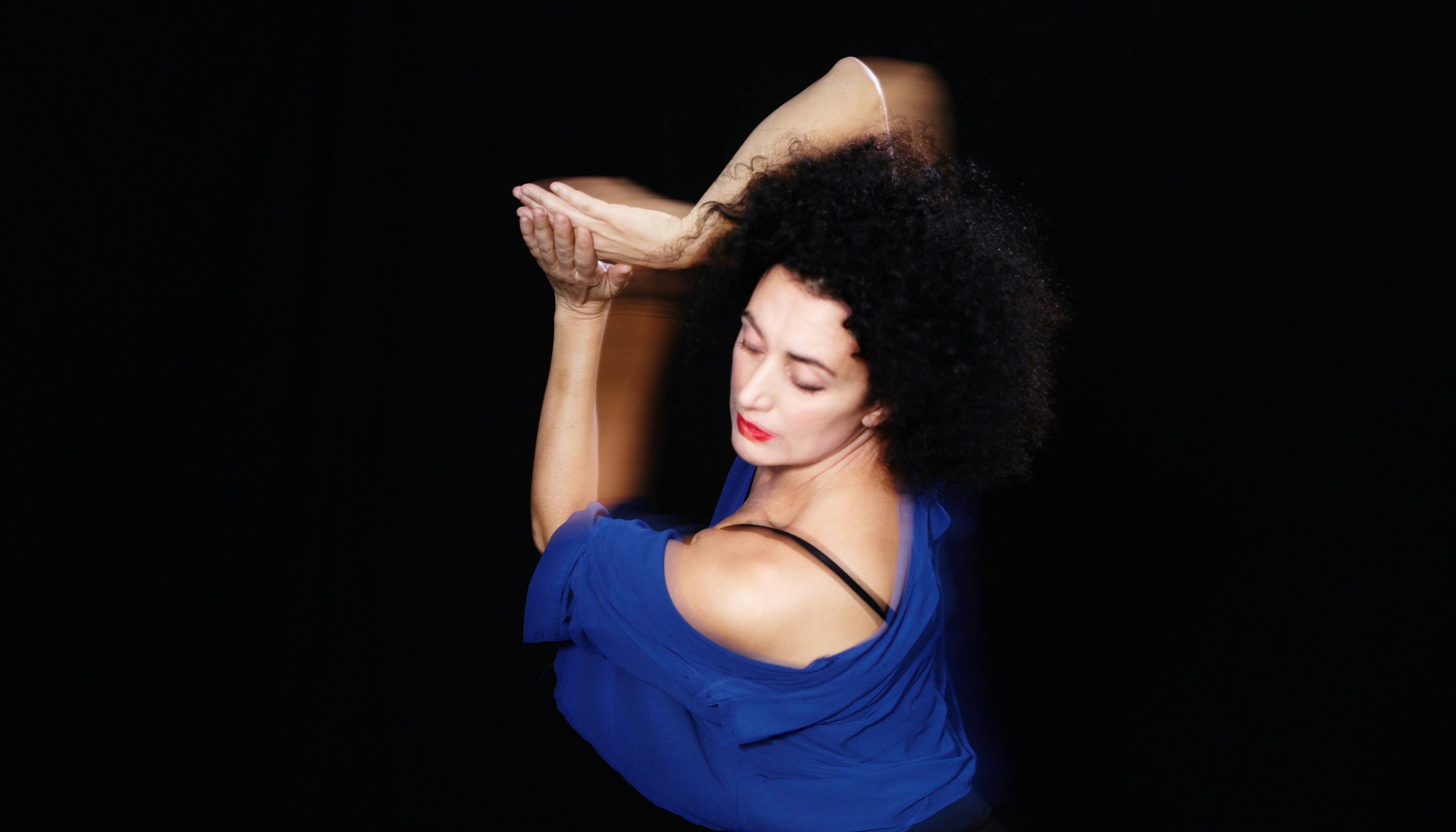 Photo on black background of Cristiana Morganti in a dance pose with her arms joined and half raised sideways