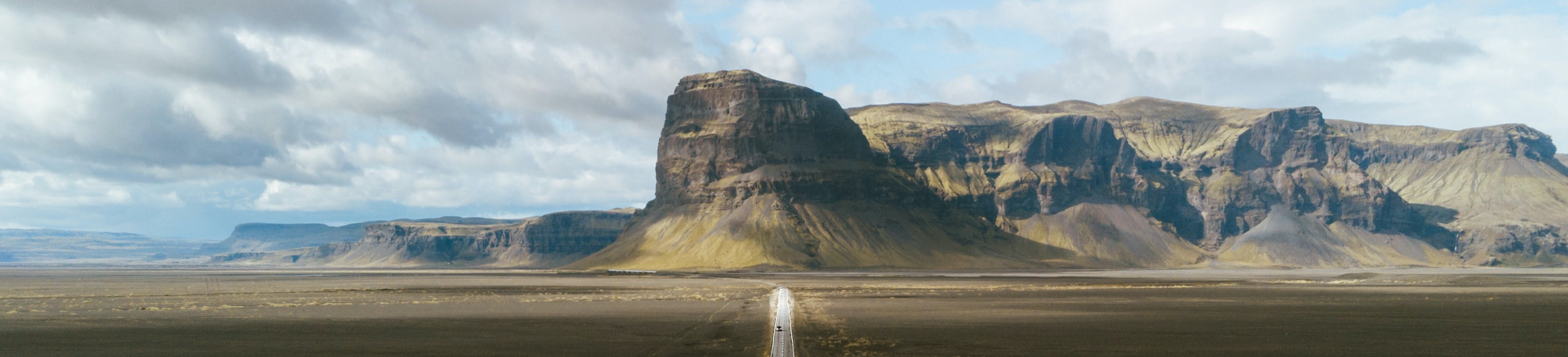 On the sides steppe, in the centre a straight road leading to a mountain range consisting of plateaus.