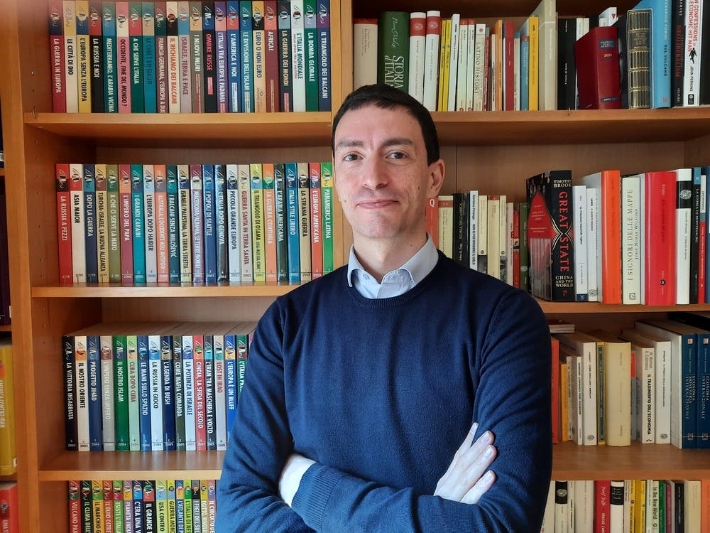 Half-length photo of Fabrizio Maronta smiling towards the camera. A bookcase in the background.
