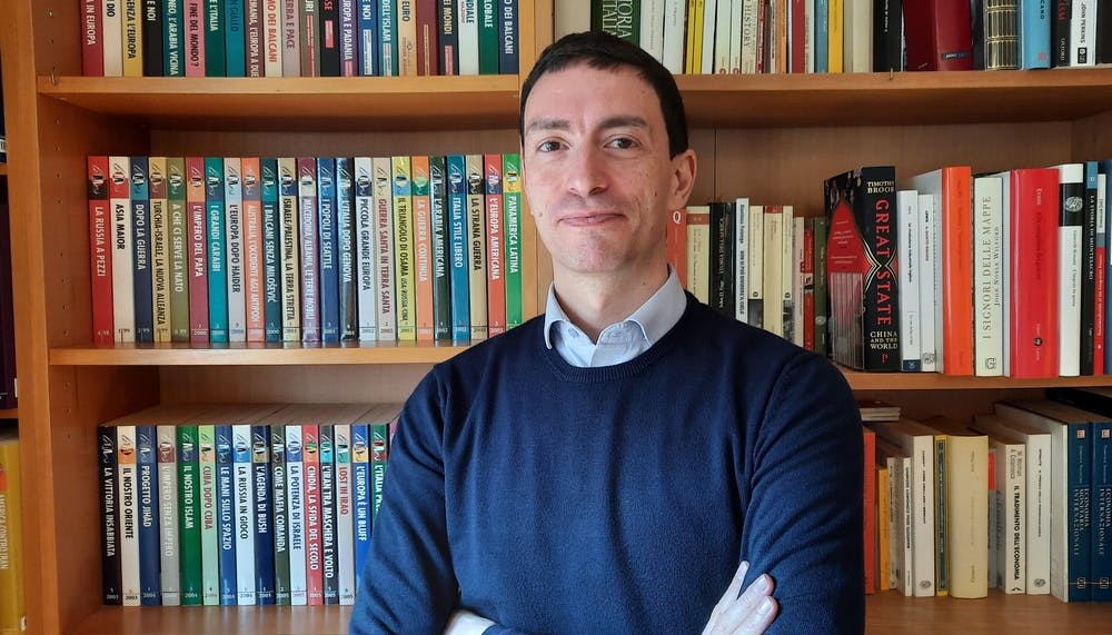 Half-length photo of Fabrizio Maronta smiling towards the camera. A bookcase in the background.