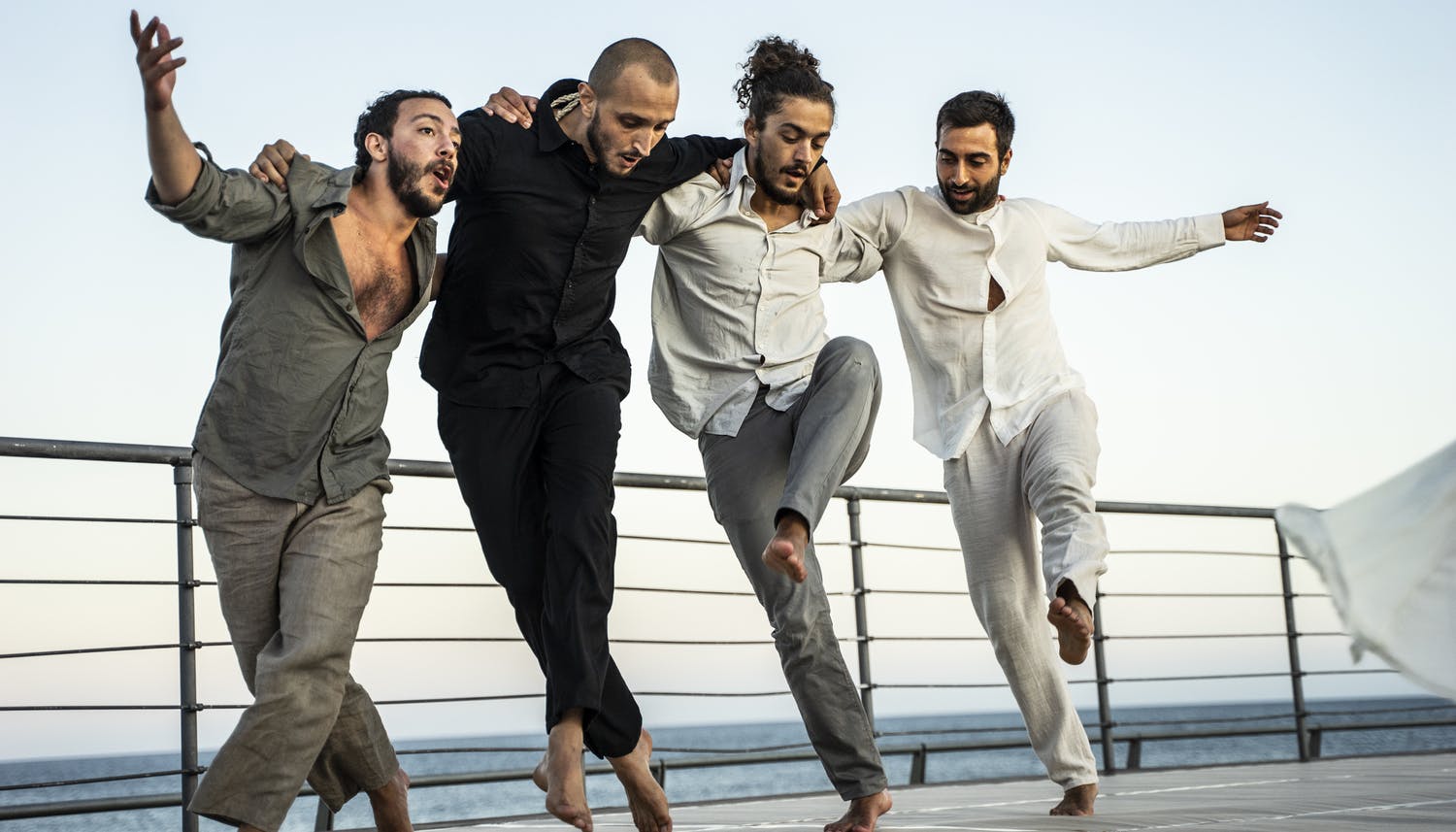 Quattro uomini sono uno a fianco dell'altro tenendosi sottobraccio. Nel ballare tengono le gambe incrociate con il piede sinistro avanti e i due danzatori laterali alzano in aria il braccio esterno.