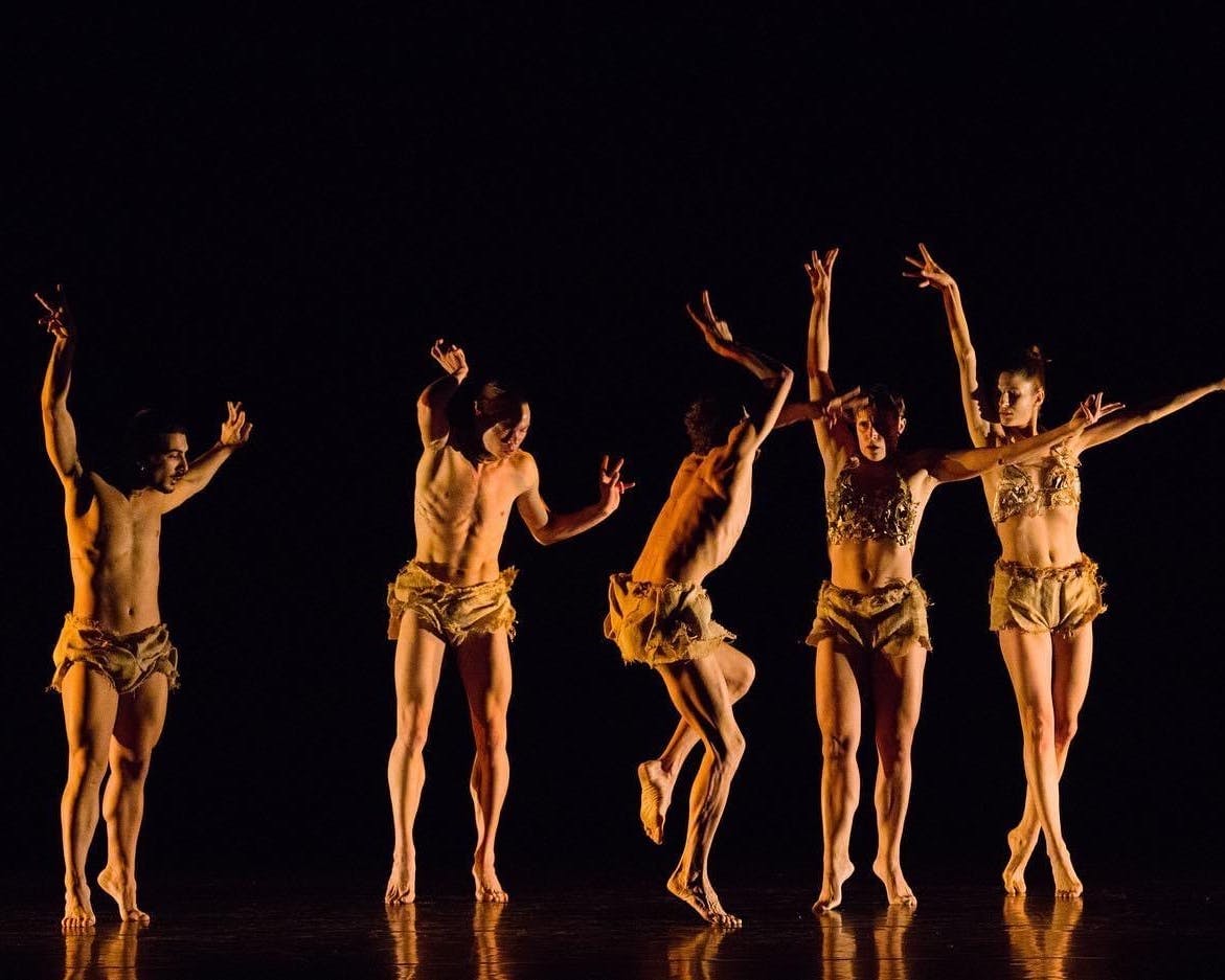 In a row, on stage, there are five dancers, each in a different pose.