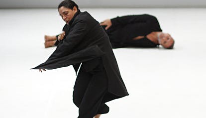 María Muñoz, in the foreground, is dancing, while Pep Ramis, behind, is lying on his side on the stage in front of the audience.