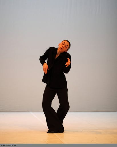 María Muñoz standing in the middle of the stage dances with her legs crossed, right foot forward, arms raised to chest height.