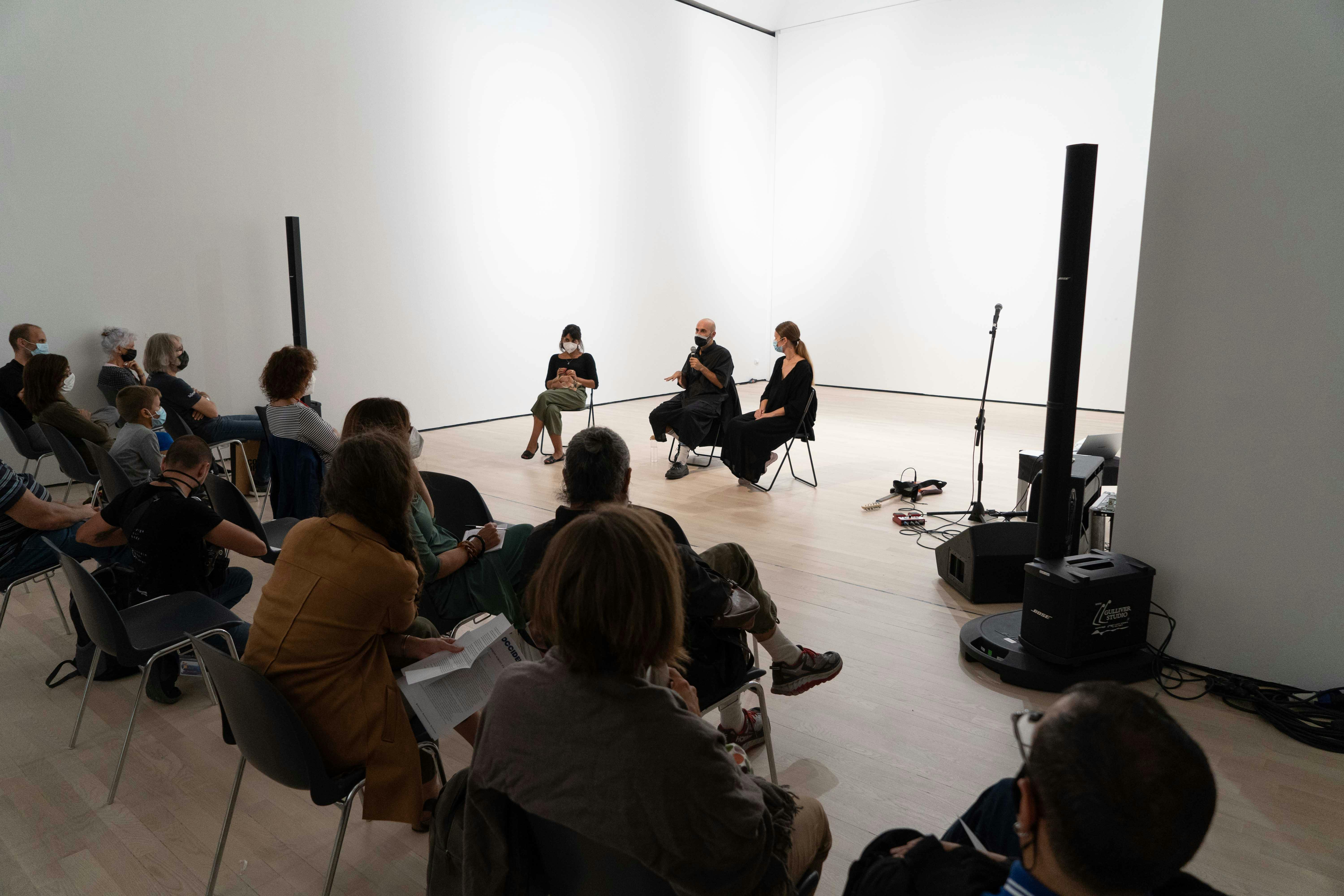 Il coreografo Daniele Ninarello, la sociologa Mariella Popolla e la drammaturga Gaia Clorilde Chernetich seduti al centro dello spazio performativo, parlano con il pubblico di fronte a loro.