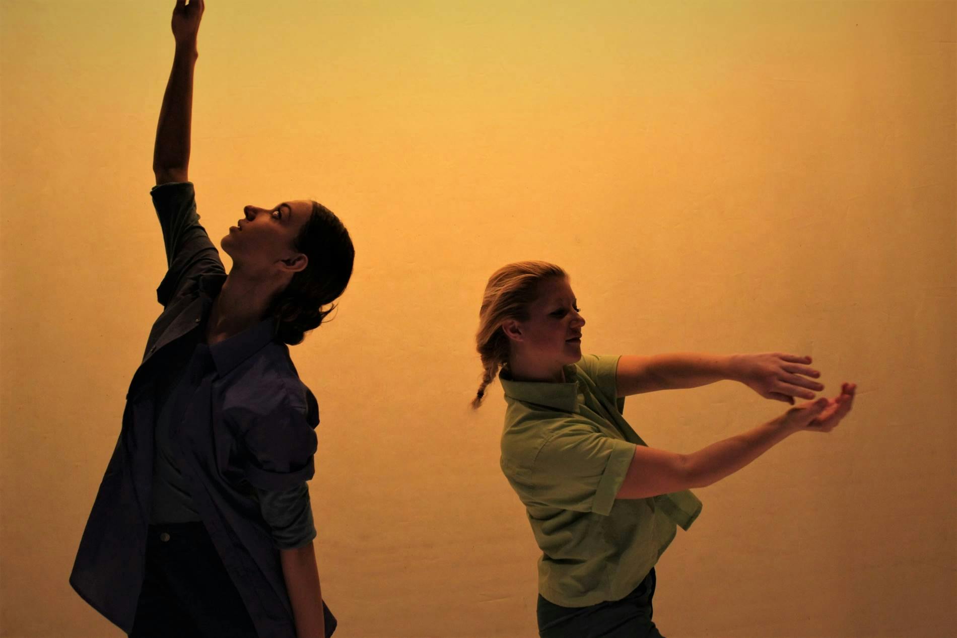 Half-bust of two dancers on orange background. One of the two, in profile, has one arm raised upward. The other, facing the opposite direction, stretches both arms loosely forward. They are wearing a blue and a teal shirt.