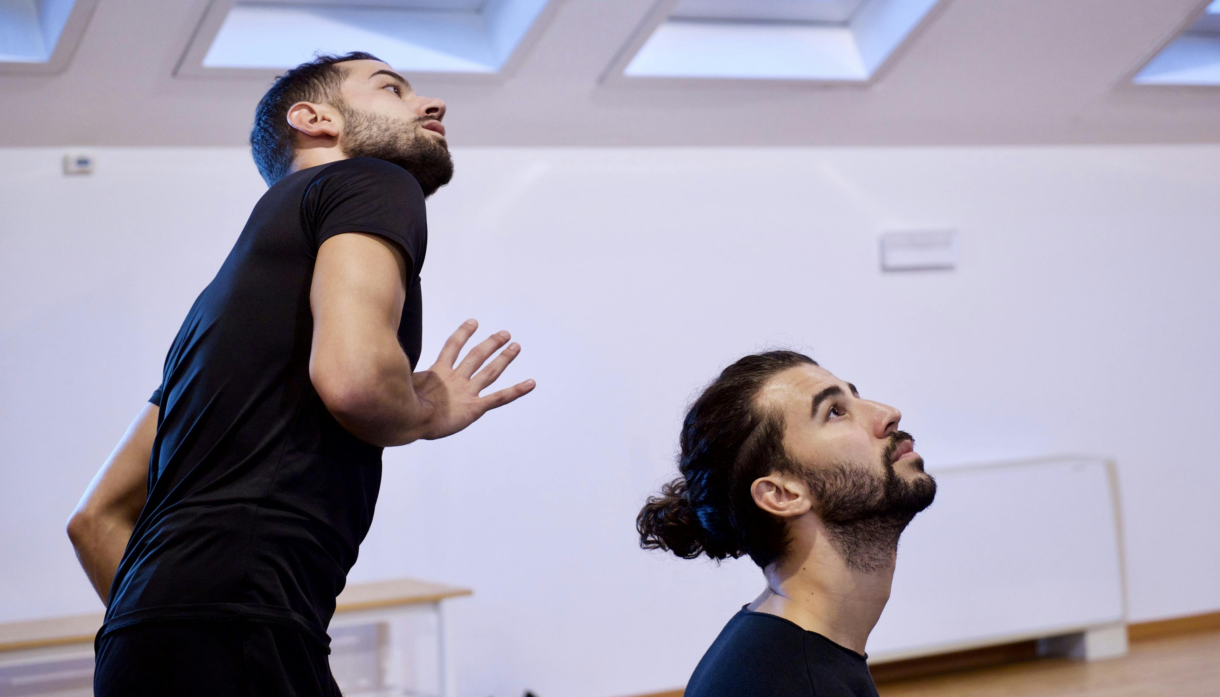 Rehearsal in the Studio. The two dancers are looking slightly upwards. They are in suits, we can see the whole upper part of one's body, only the head and shoulders of the other.