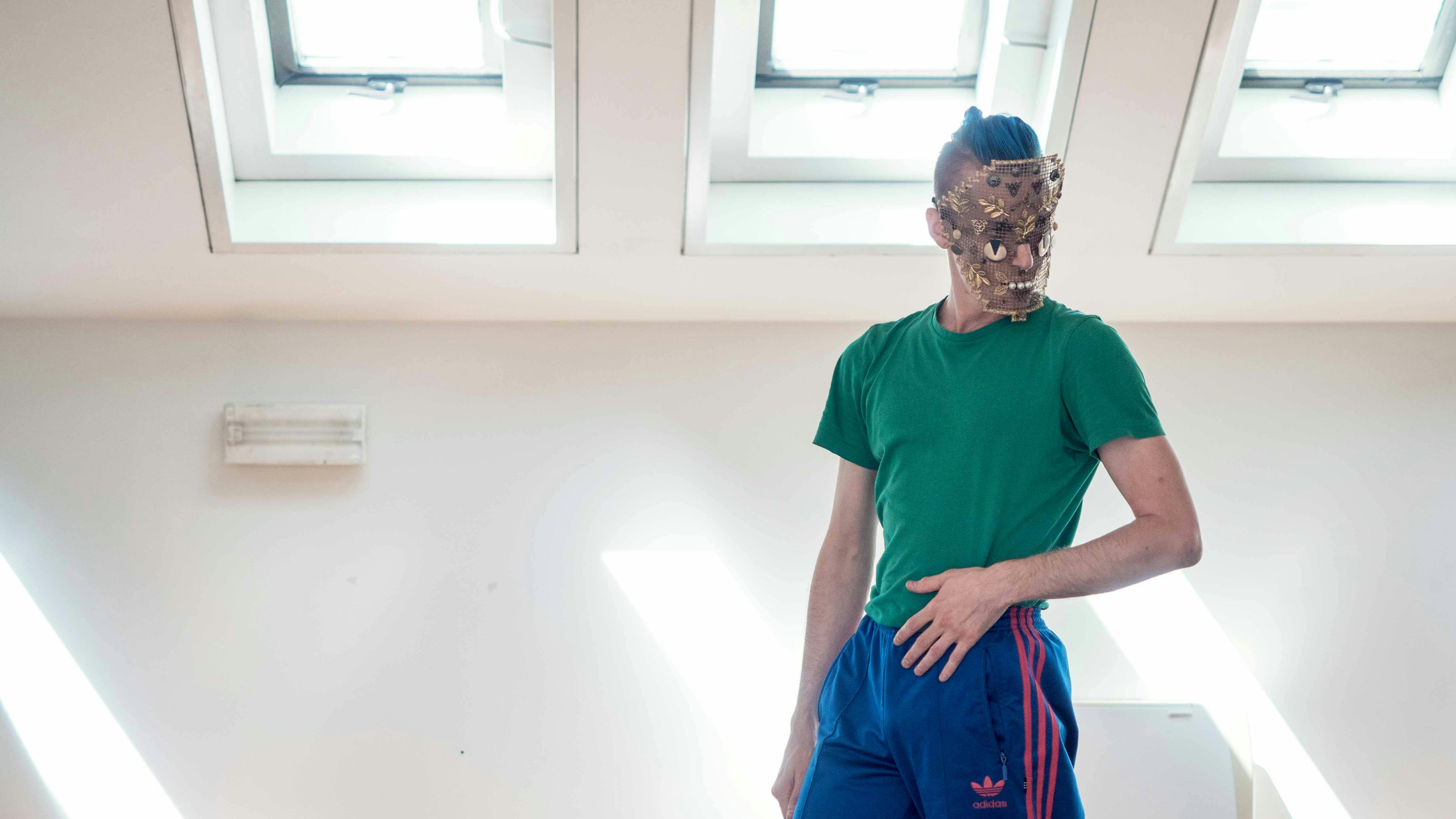 Nicola Galli, in the Studio, wearing one of his masks from "Il mondo altrove". He's dressed in a forensic green shirt and a blue jumpsuit.
