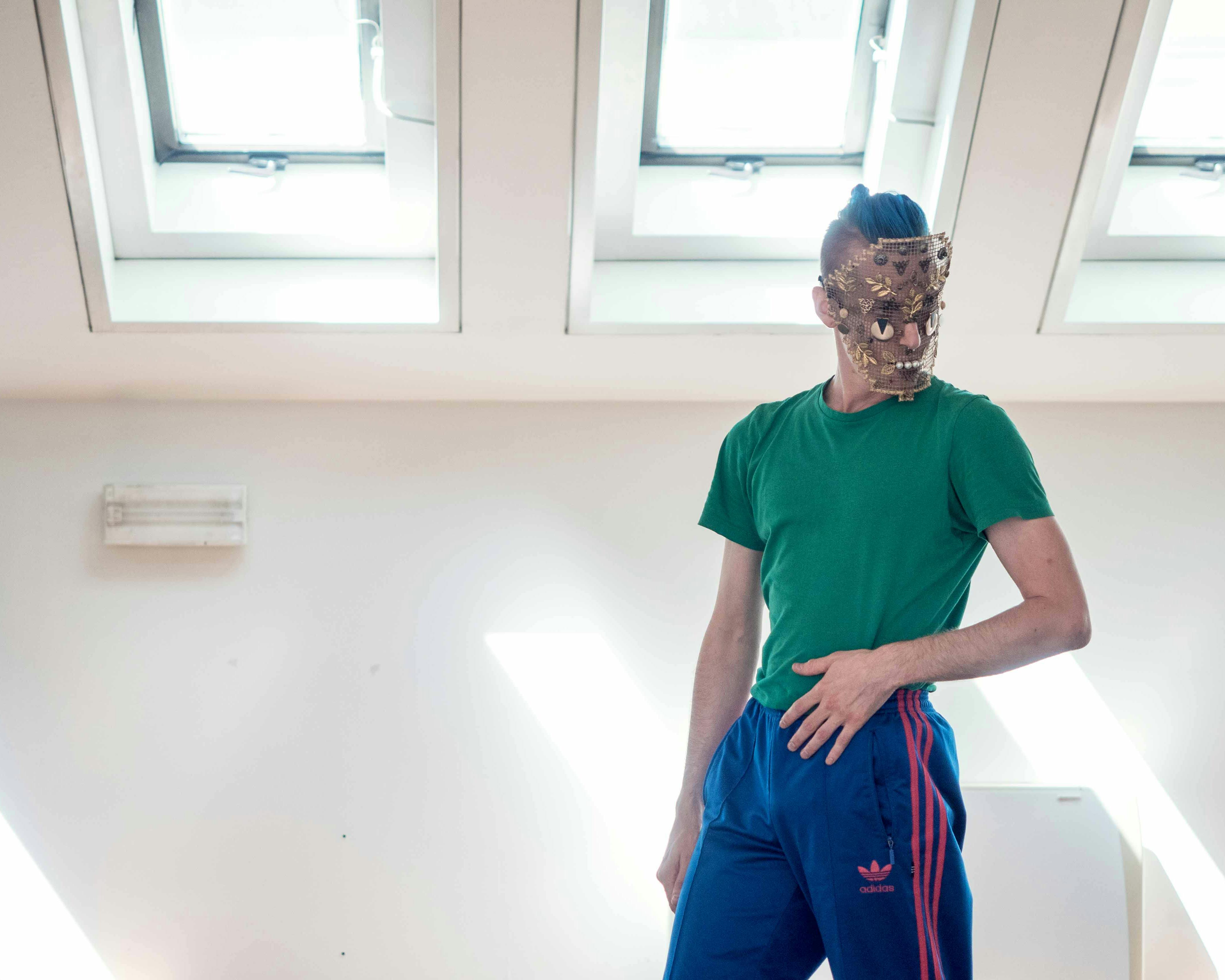 Nicola Galli, in sala, con addosso una delle maschere di "Il mondo altrove". Indossa una maglia verde foreesta e una tuta blù.