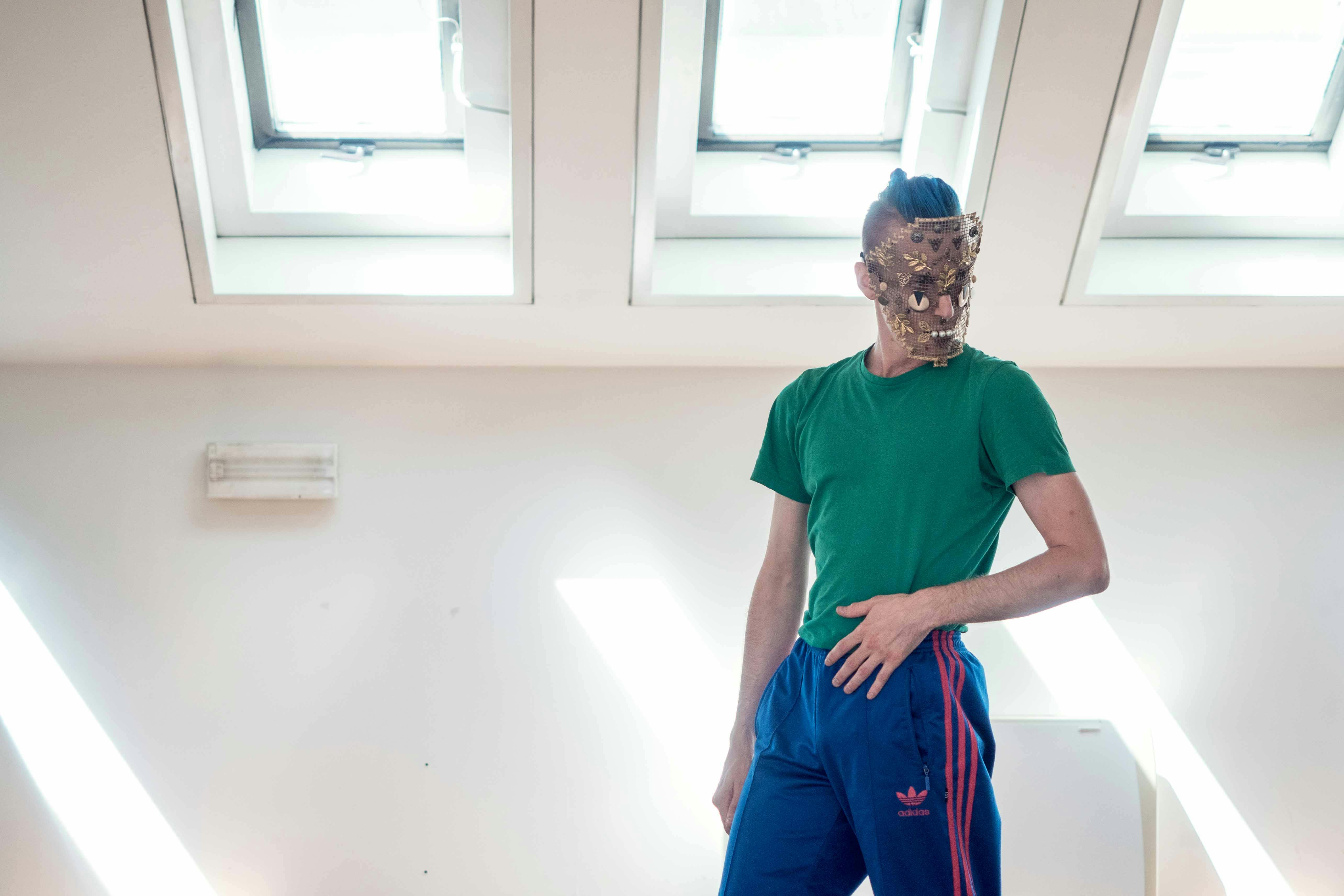 Nicola Galli, in the Studio, wearing one of his masks from "Il mondo altrove". He's dressed in a forensic green shirt and a blue jumpsuit.