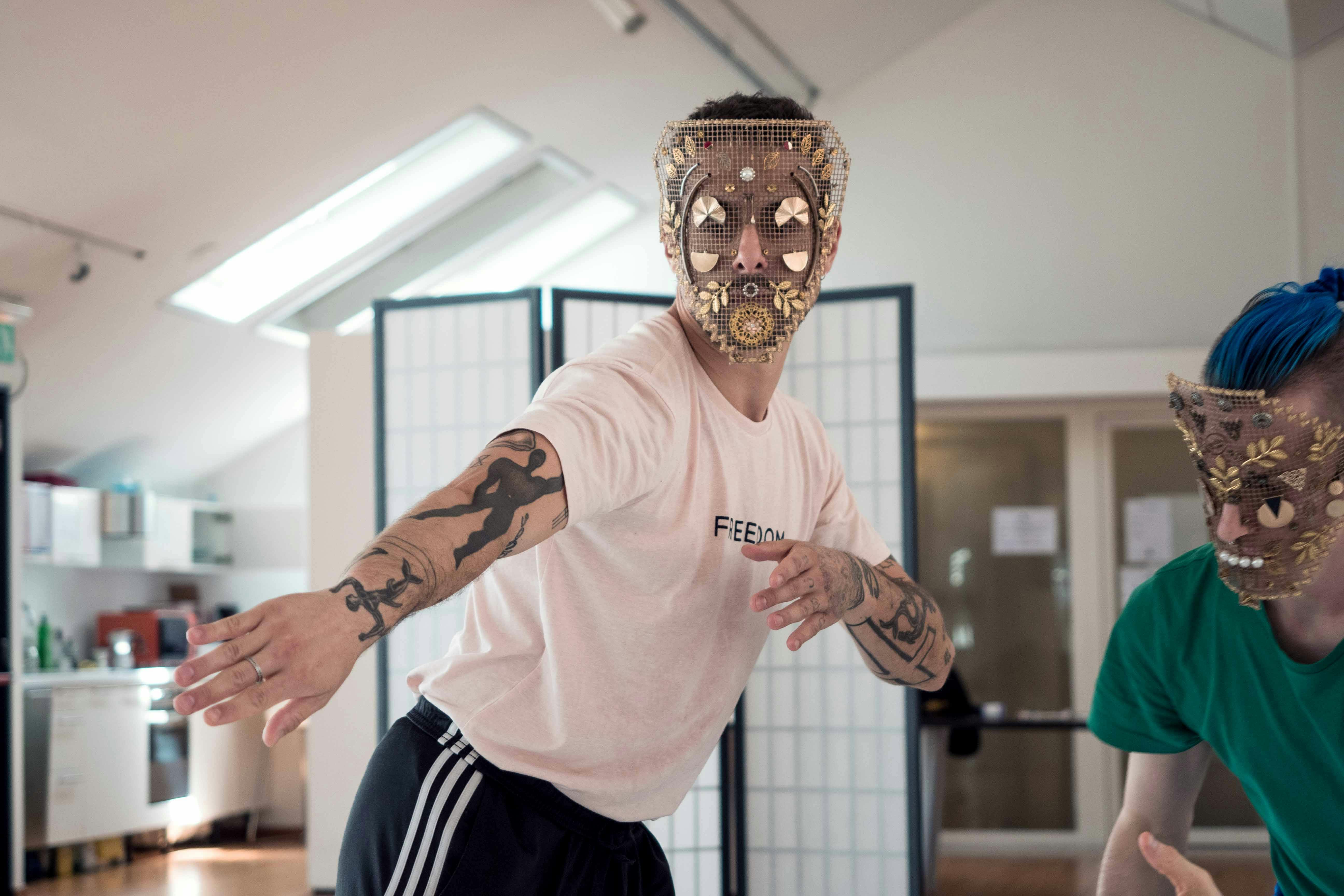 Two dancers in rehearsal. Both wear a reticulated mask, decorated with gold and steel leaves, foils and shapes. 