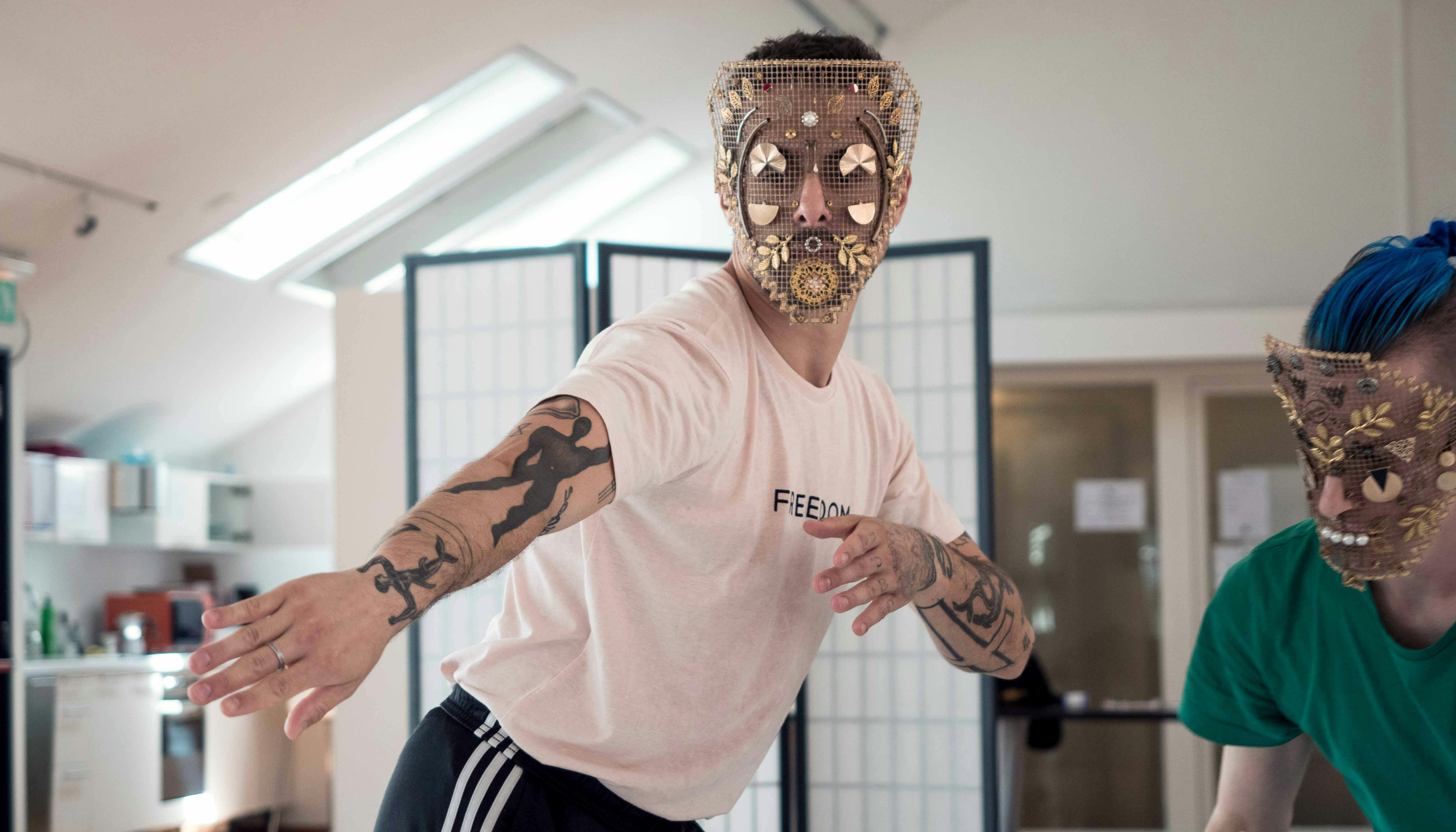 Two dancers in rehearsal. Both wear a reticulated mask, decorated with gold and steel leaves, foils and shapes. 