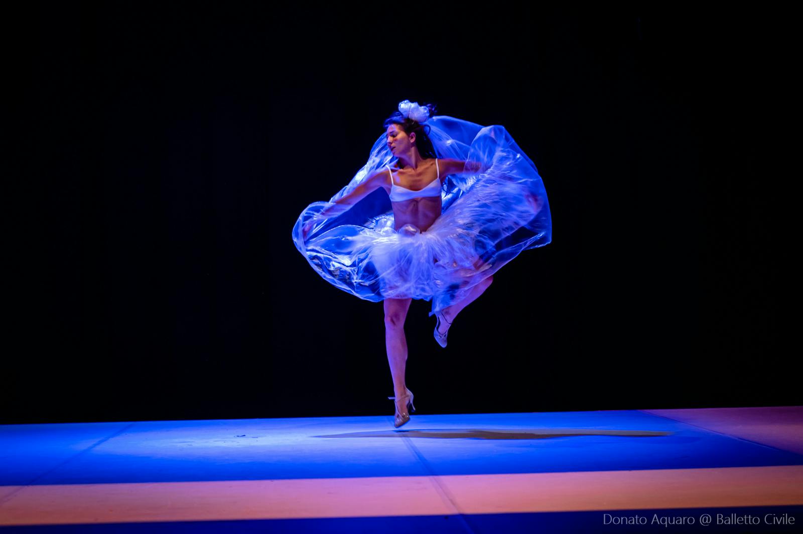 Una ballerina classica, con un'ampia gonna in nylon, danza sulla punta del piede destro. La gamba sinistra, piegata, è indirizzata verso l'altra gamba.