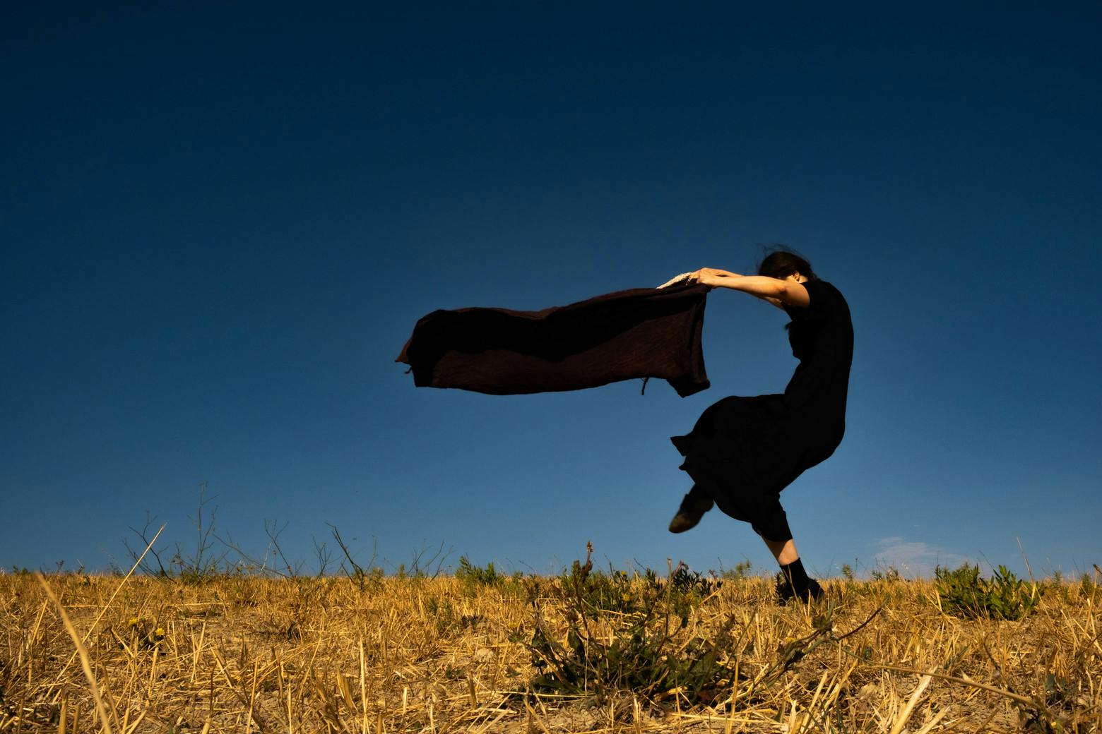 A woman, seen from the side, walks backwards while arching her back forward. With her arms outstretched forward she holds a cloth that flutters horizontally for movement.