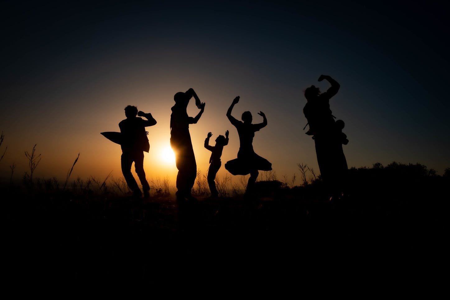At sunset, five dancers are dancing in various poses against the light.