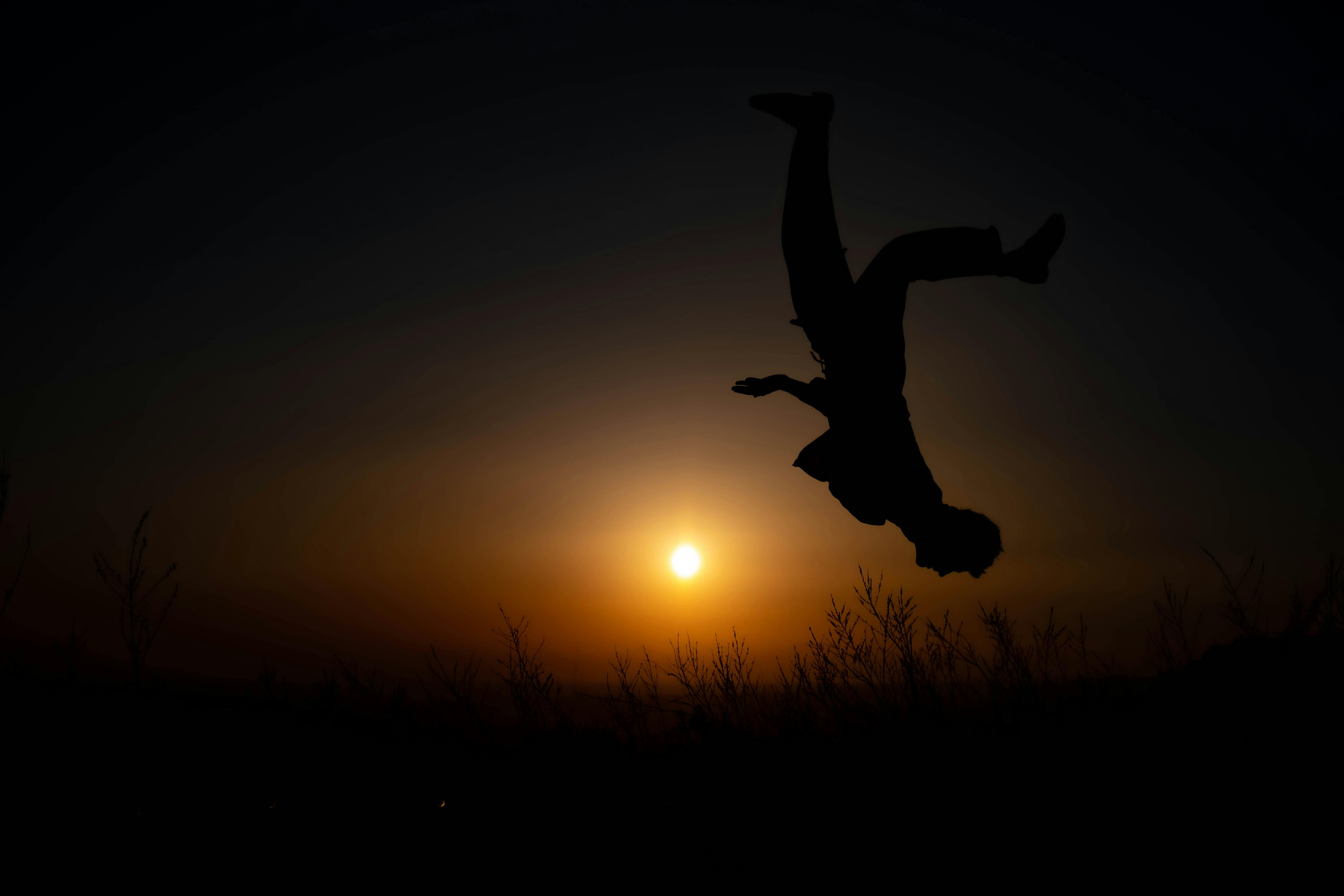 At sunset and against the light, a man is upside down doing a somersault.