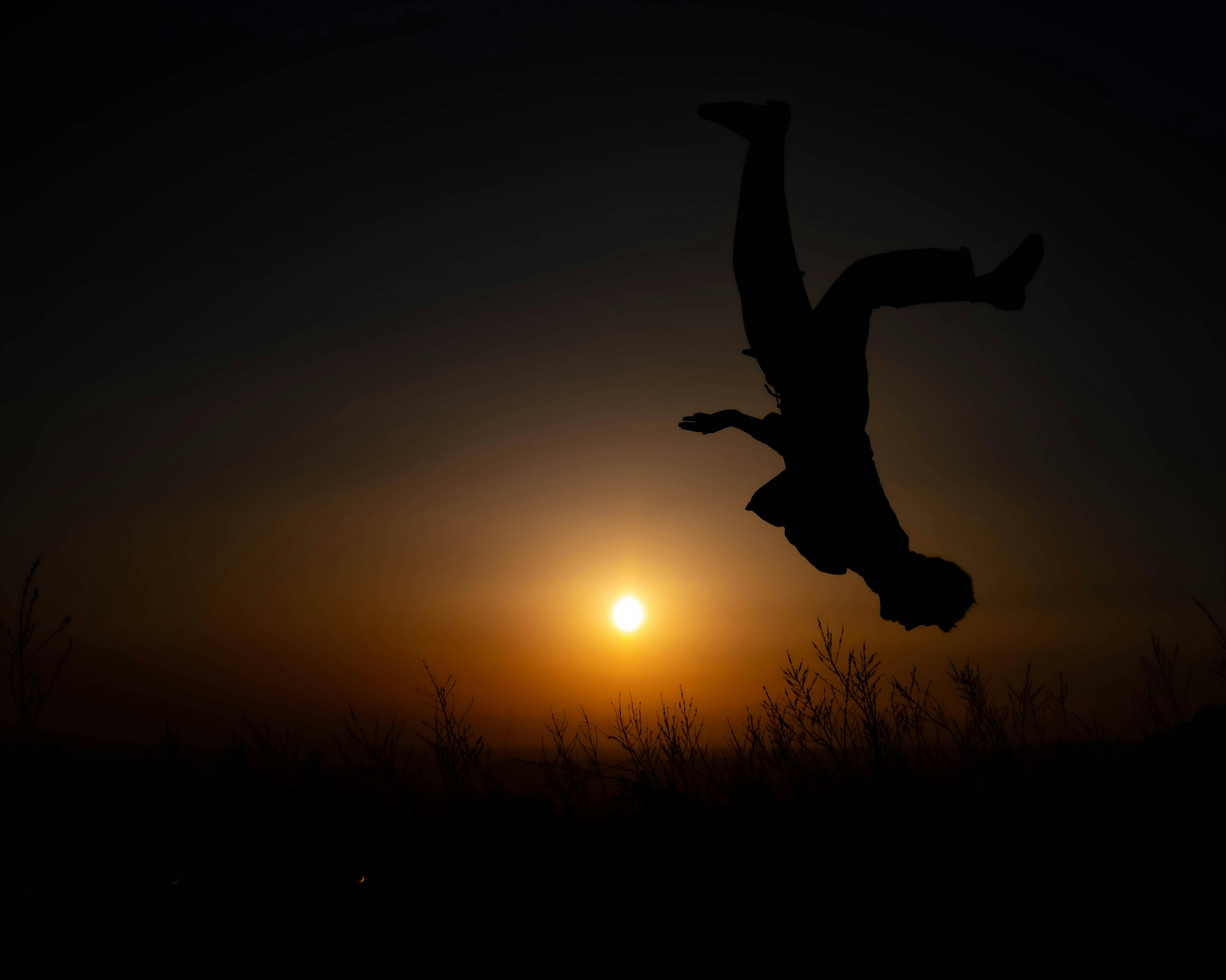 Al tramonto e in controluce, un uomo è a esta in giù mentre sta facendo un salto mortale.
