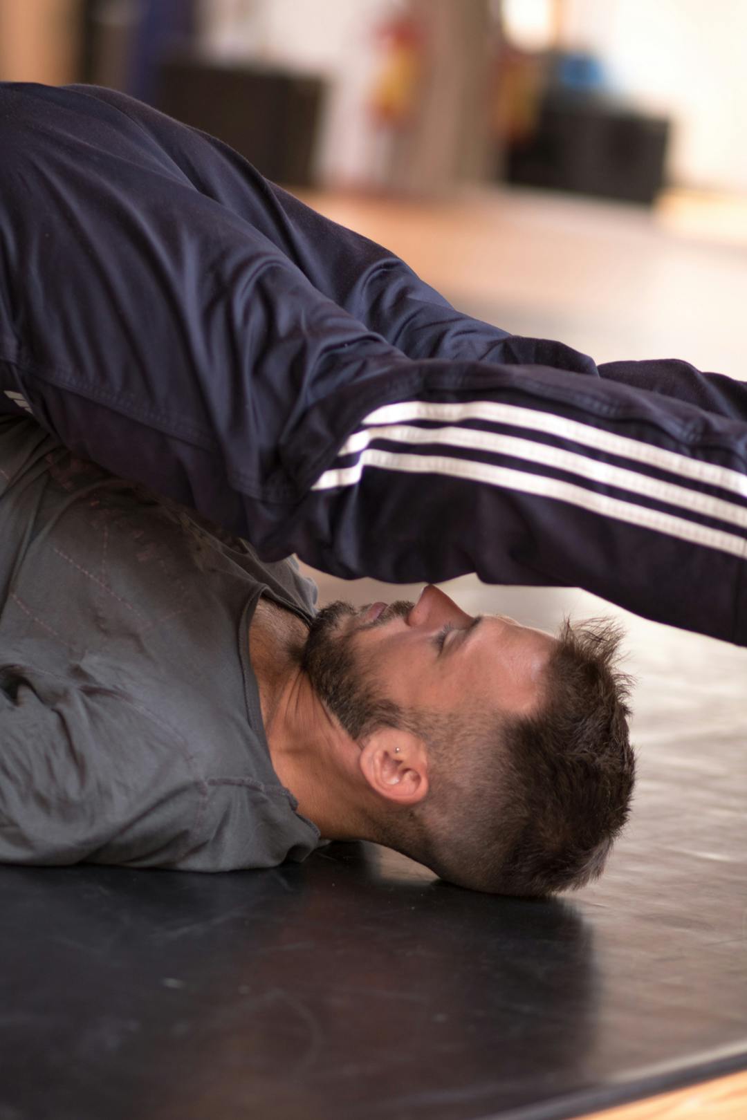 Un danzatore durante il riscaldamento in sala. È sdraiato a terra e solleva gambe e bacino oltre la propria testa.