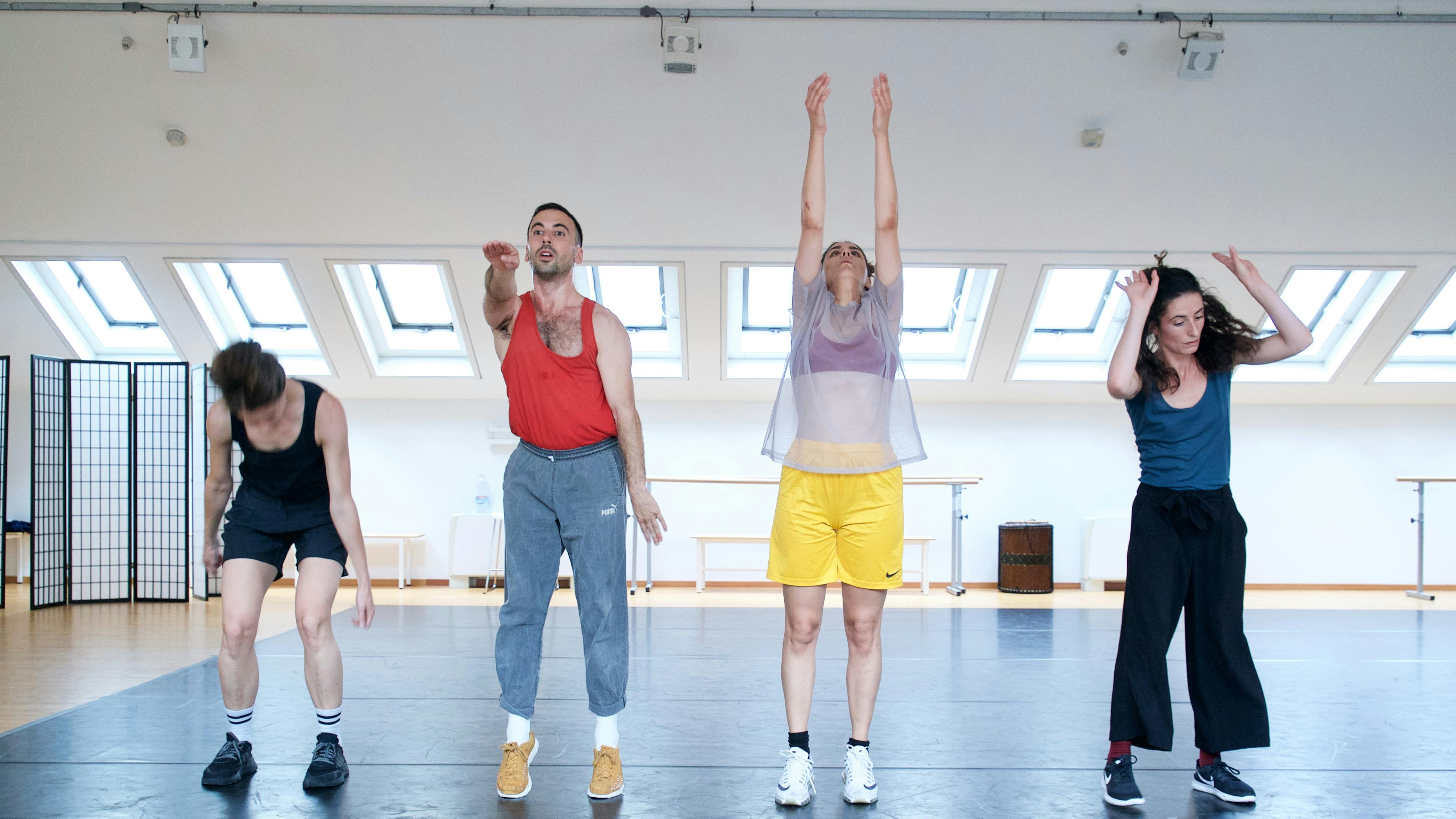 Four performers in a horizontal row in the Studio make different movements with their arms
