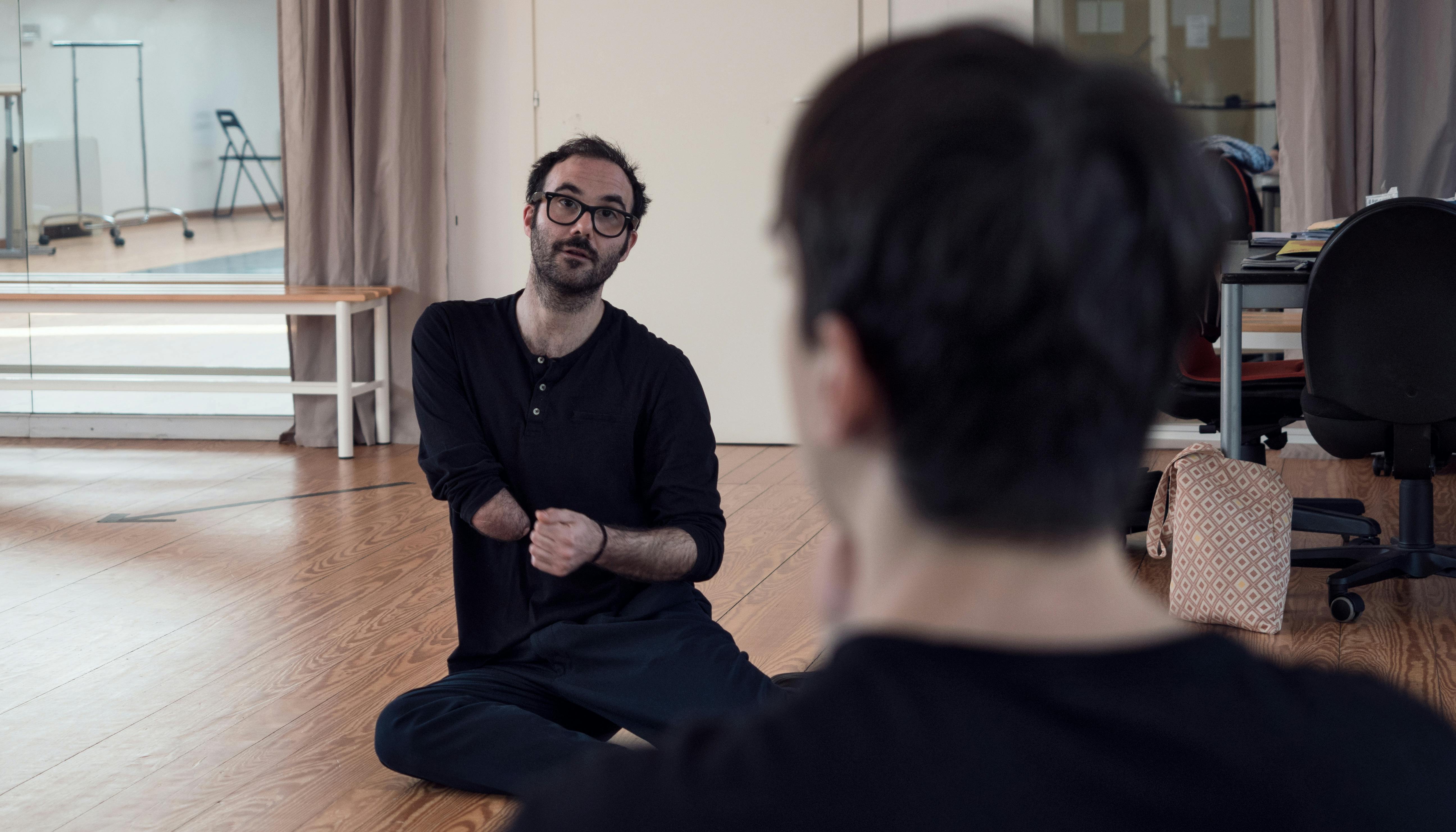 Aristide Rontini, seduto a terra nello Studio, parla al danzatore Cristian Cucco, seduto di fronte a lui.