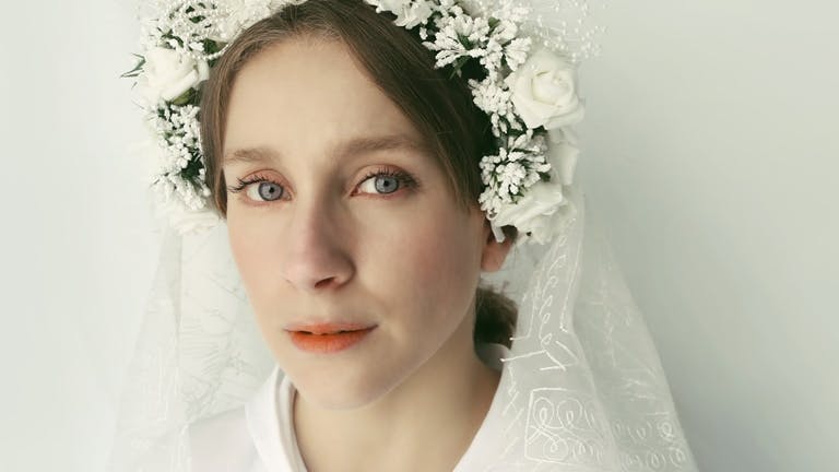 Una ragazza in primo piano con fiori in testa bianchi e velo