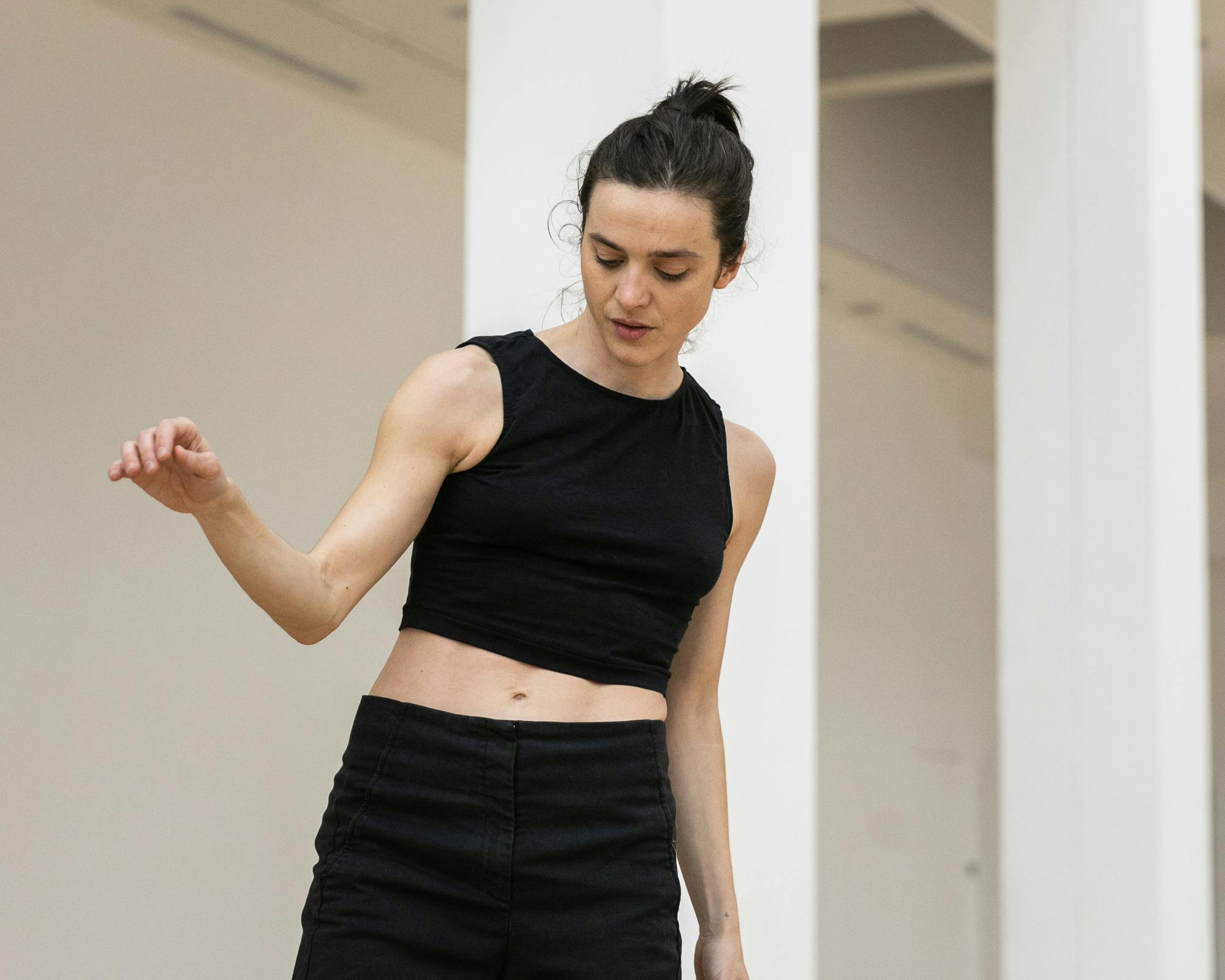 Annamaria Ajmone in rehearsal. She is wearing a black tank top and dark pants and is raising her right arm, bent, to shoulder height.