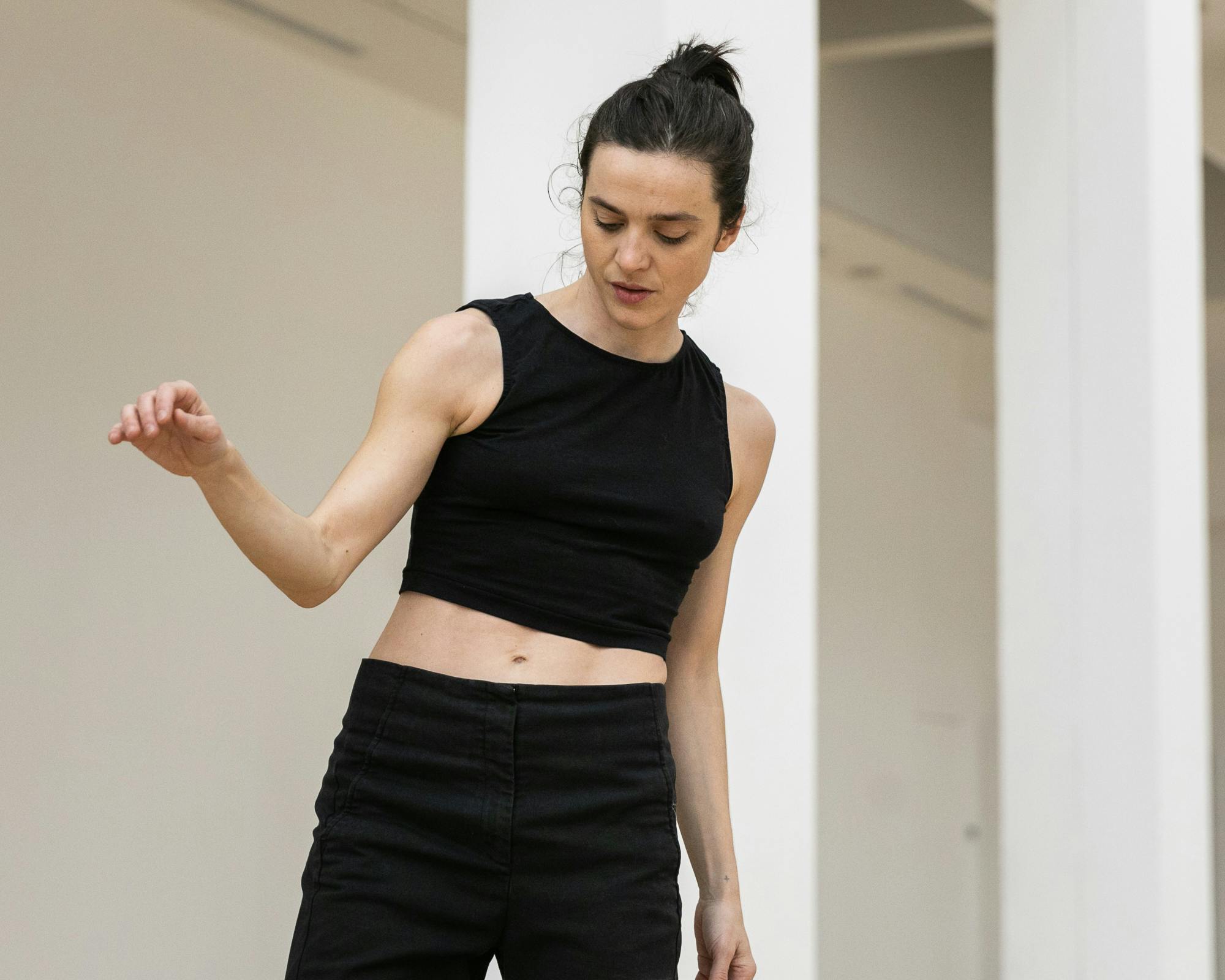 Annamaria Ajmone in rehearsal. She is wearing a black tank top and dark pants and is raising her right arm, bent, to shoulder height.