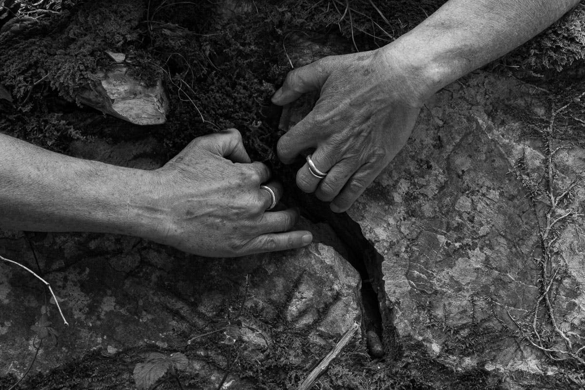 Foto in bianco e nero. Esterno; due mani afferrano una crepa nel terreno tirando come a volerla allargare.