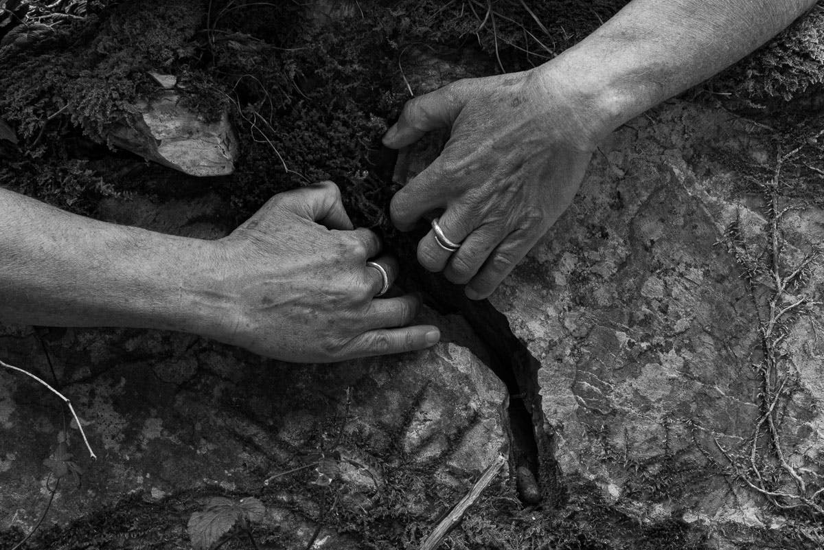 Photo in black and white. Exterior; two hands grasp a crack in the ground pulling as if to widen it.