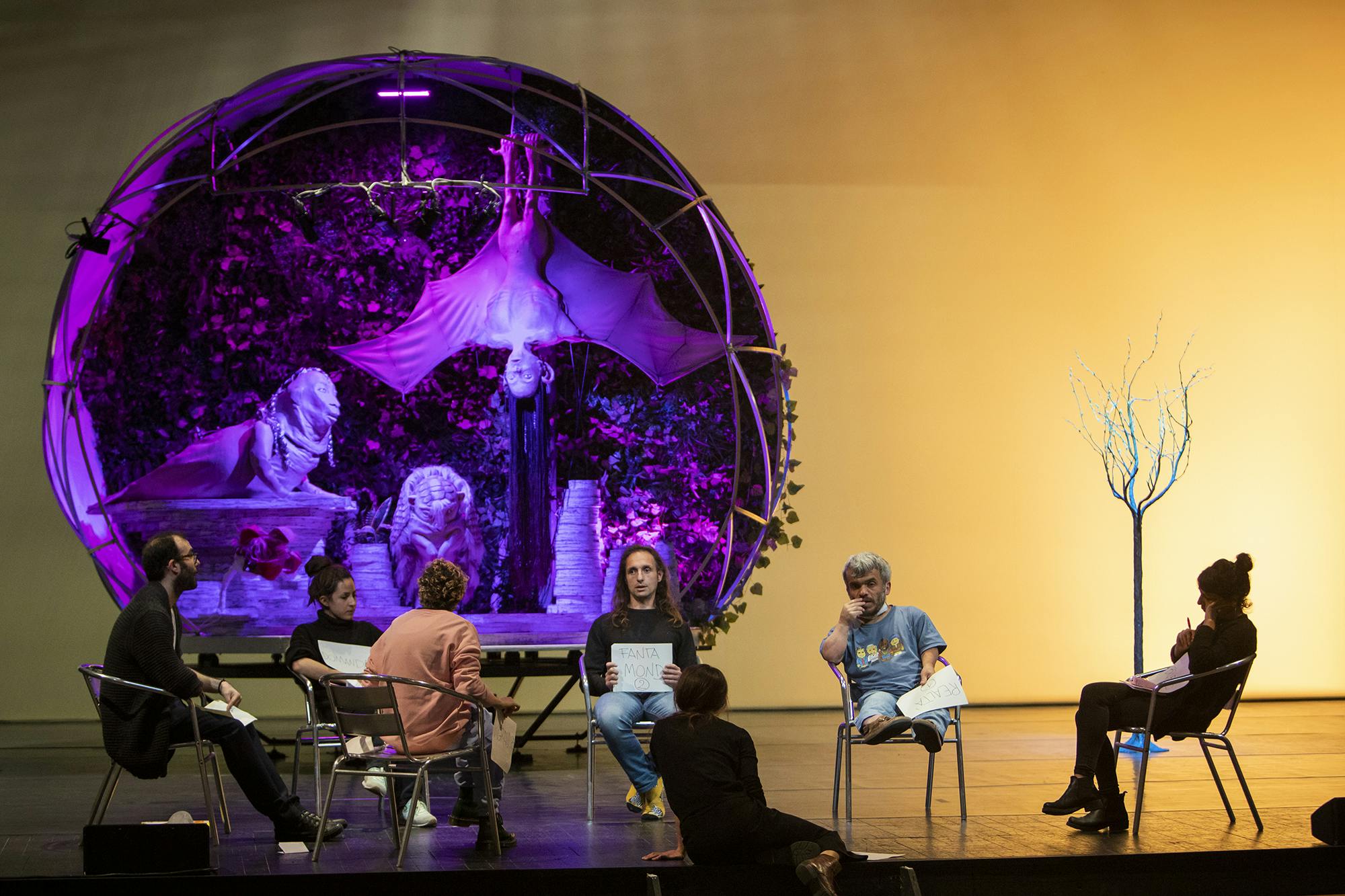 Al.Di.Qua.Artists and Marta Cuscunà sitting in a circle on a stage while discussing the project. Behind them there is the original set design of Earthbound.