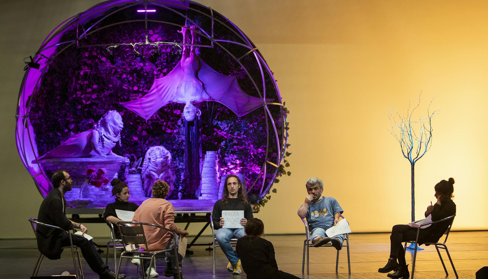 Al.Di.Qua.Artists and Marta Cuscunà sitting in a circle on a stage while discussing the project. Behind them there is the original set design of Earthbound.