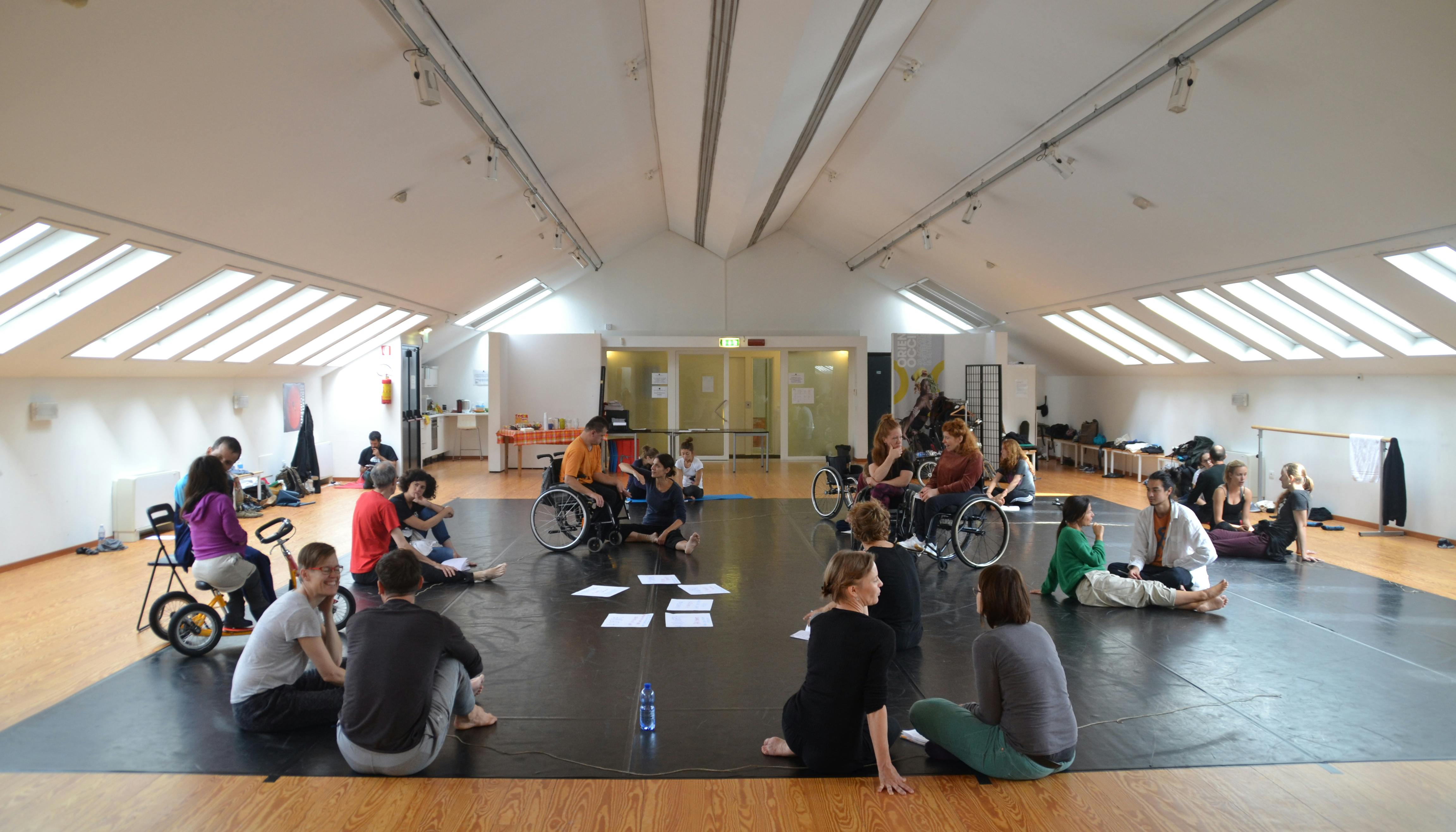 Un gruppo di persone con e senza disabilità discutono a coppie nello Studio di Oriente Occidente durante un laboratorio.