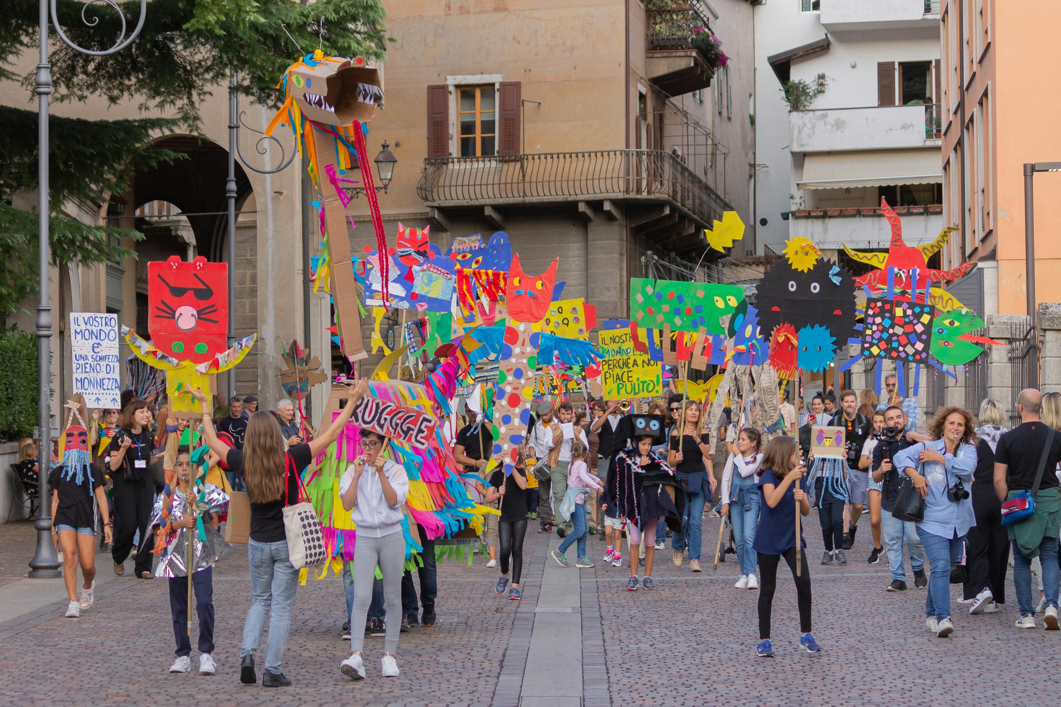 Una parata di giovanissimi nelle strade di Rovereto. Hanno cartelli molto colarati realizzati con l'artista e marciano per l'attenzine all'ambiente