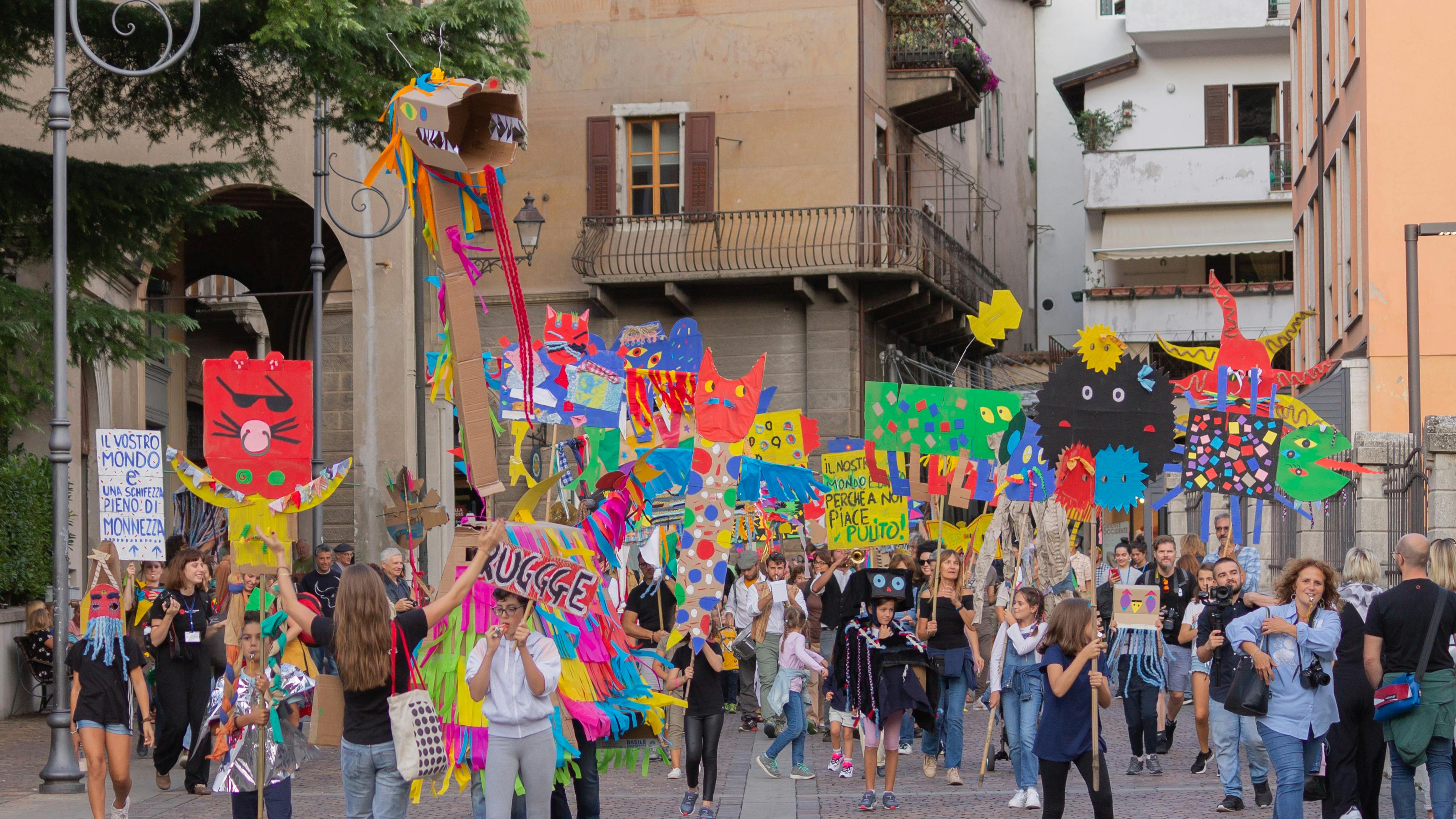 A parade of young people in the streets of Rovereto. They carry colourful signs made by the artist and march for environmental awareness.