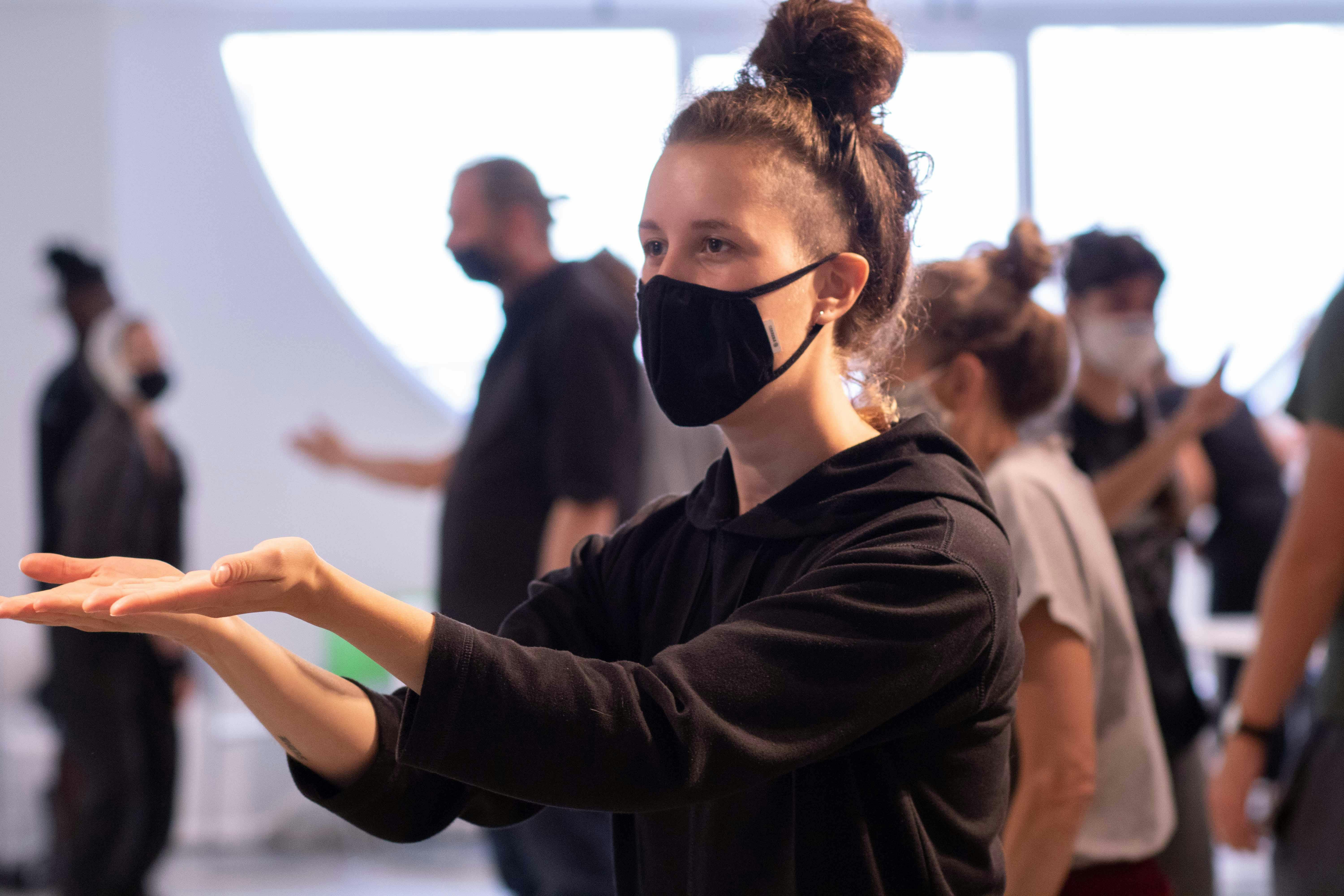 Lab participants, standing in space, practicing Lis signs in movement. In the foreground, a participant raises both arms forward, palms facing up. 