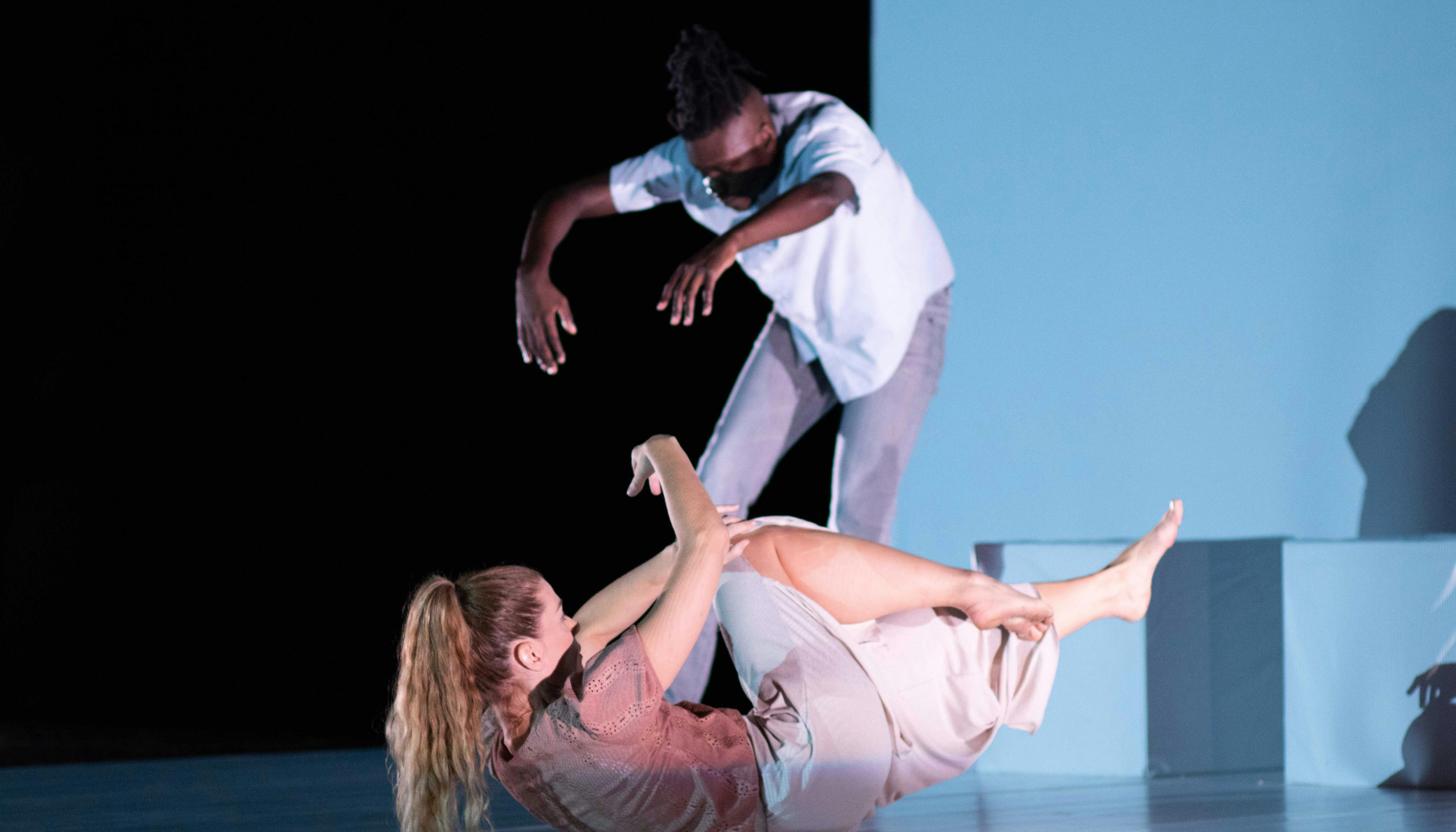 Sarah Bockers and Dodzi Dougban on stage during the preformance Gravity.  She is with her back to the floor, arms and legs raised off the stage; he is standing, with his back in contraction and his arms extended forward.