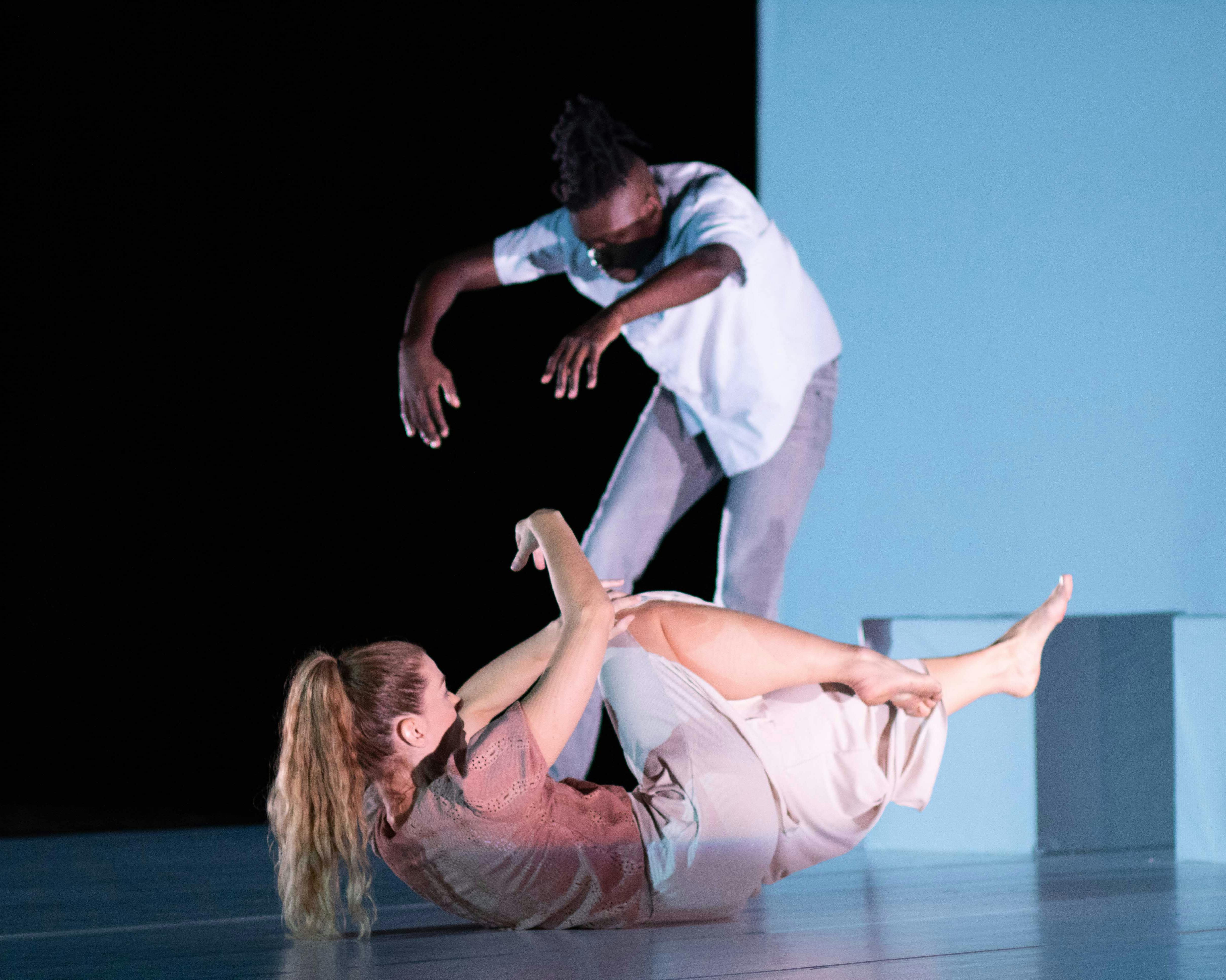 Sarah Bockers and Dodzi Dougban on stage during the preformance Gravity.  She is with her back to the floor, arms and legs raised off the stage; he is standing, with his back in contraction and his arms extended forward.