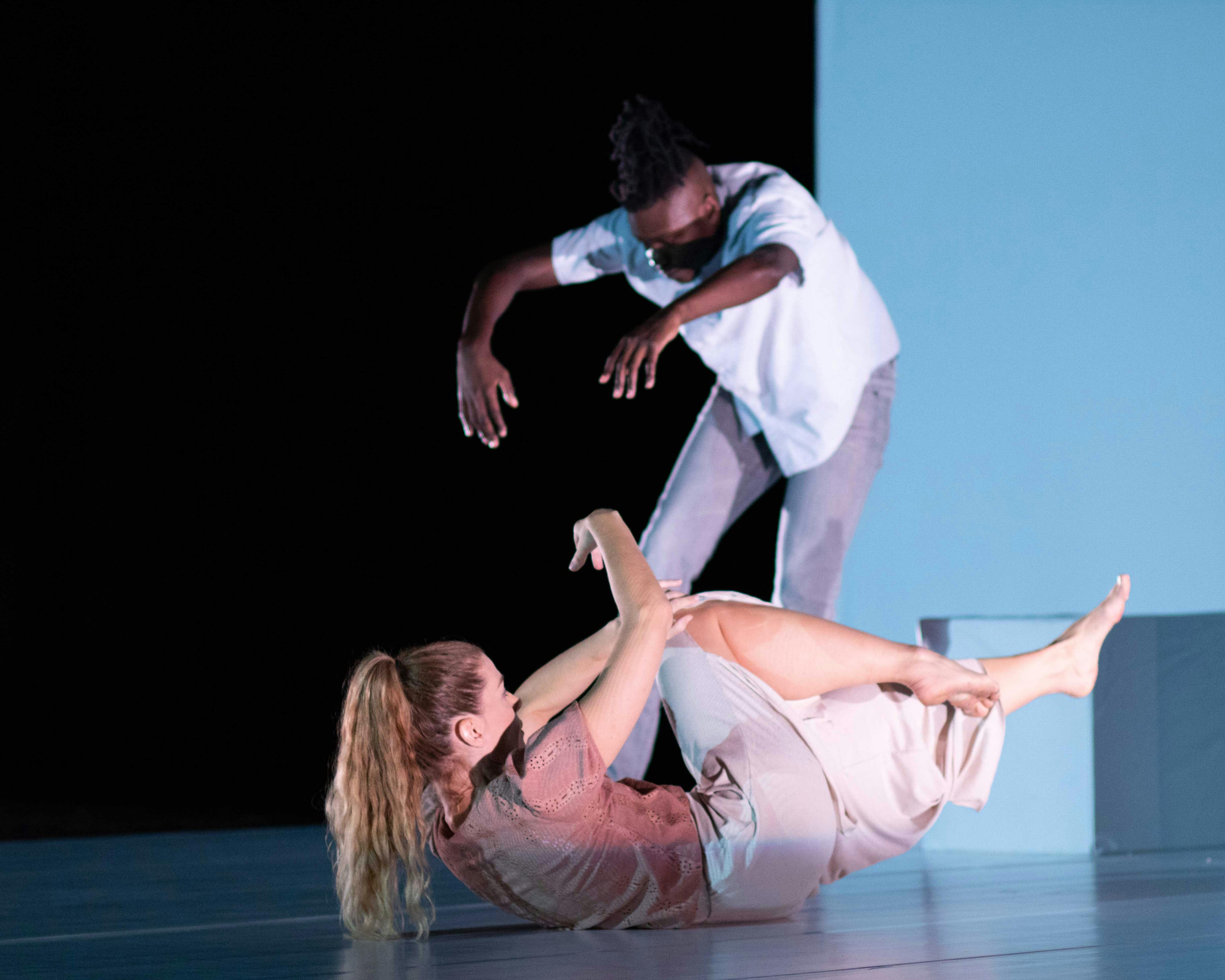 Sarah Bockers e Dodzi Dougban sul palco durante la performance Gravity.  Le è con la schiena a terra, braccia e gambe sollevate dal palco; lui è in piedi, con la schiena in contrazione e le braccia allungate in avanti.