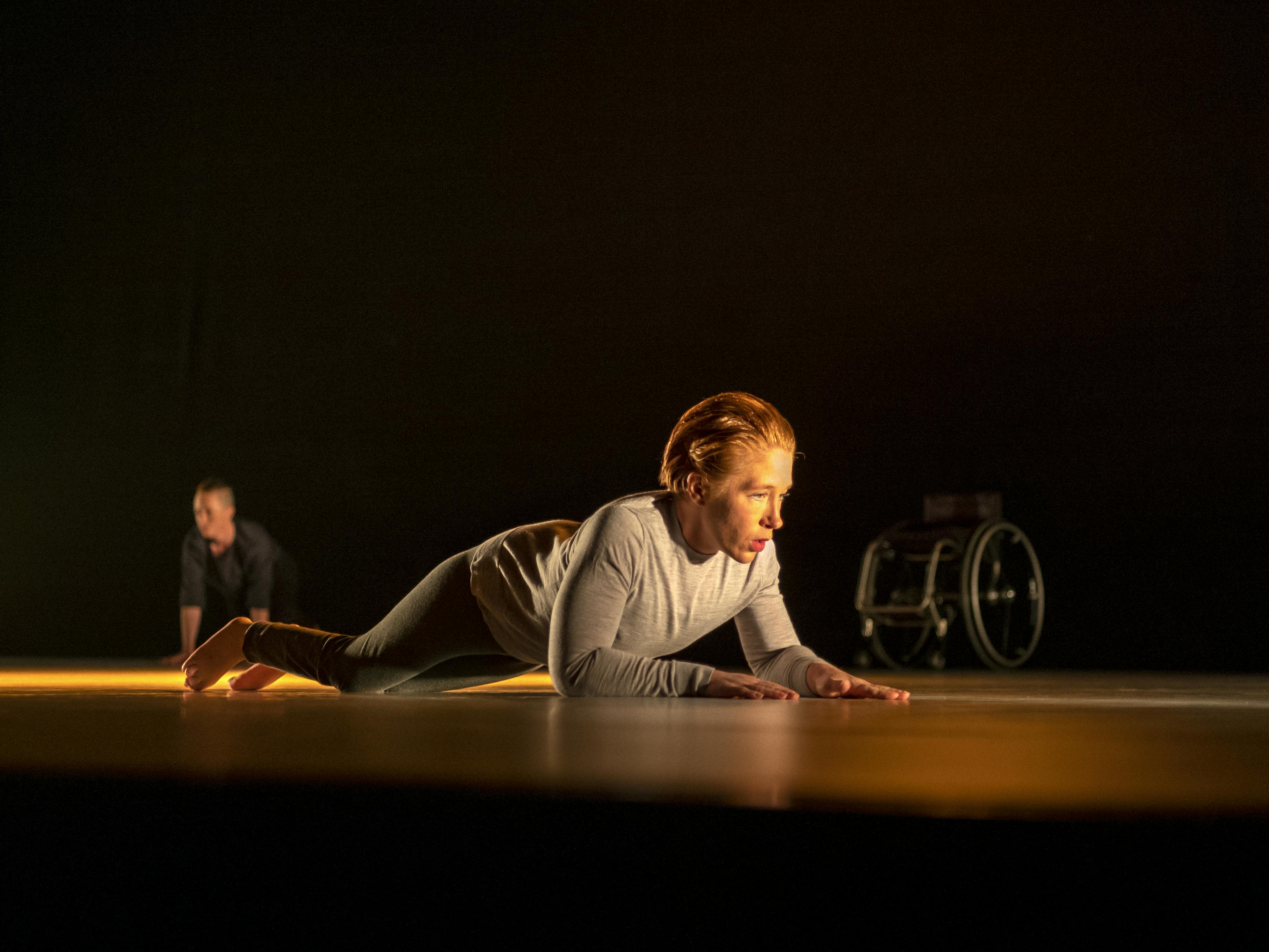 Felicia Sparrström as she crosses the stage during the Moby Dick performance. She is illuminated by a warm light. In the background, also on stage, a wheelchair can be glimpsed.