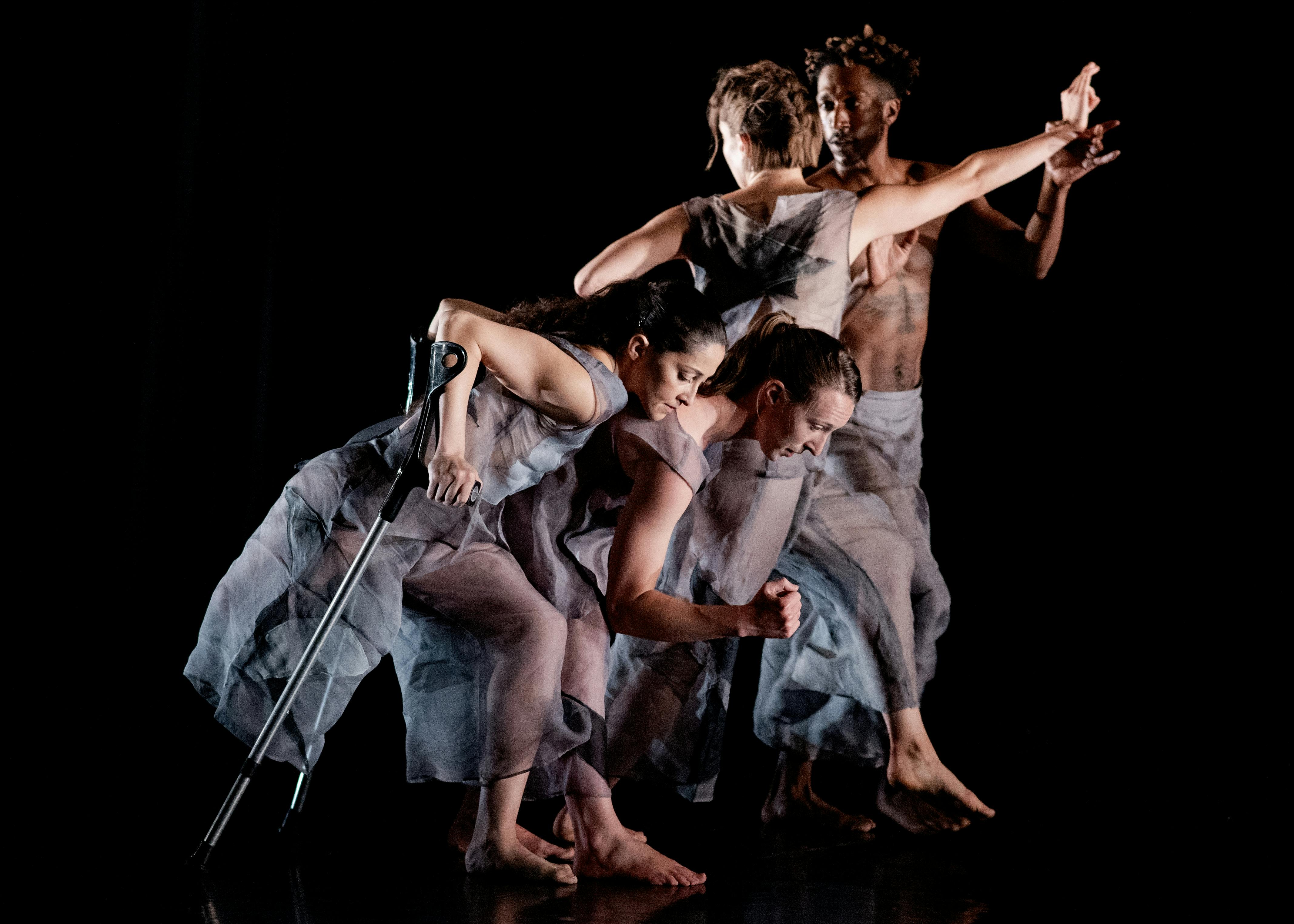 Un gruppo di danzatori in scena. In primo piano una danzatrice con una stampella.