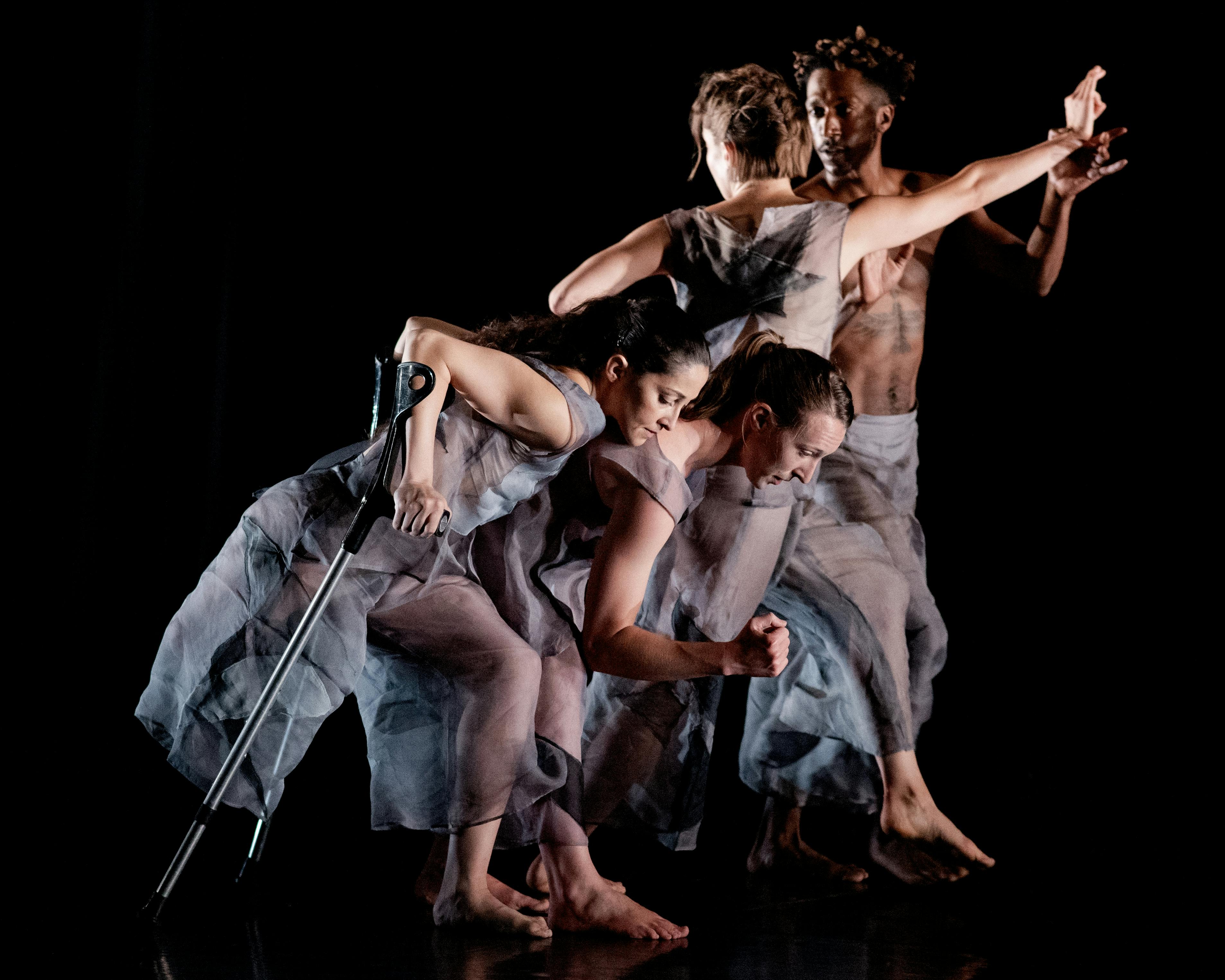 A group of dancers on stage. In the foreground a dancer with a crutch.