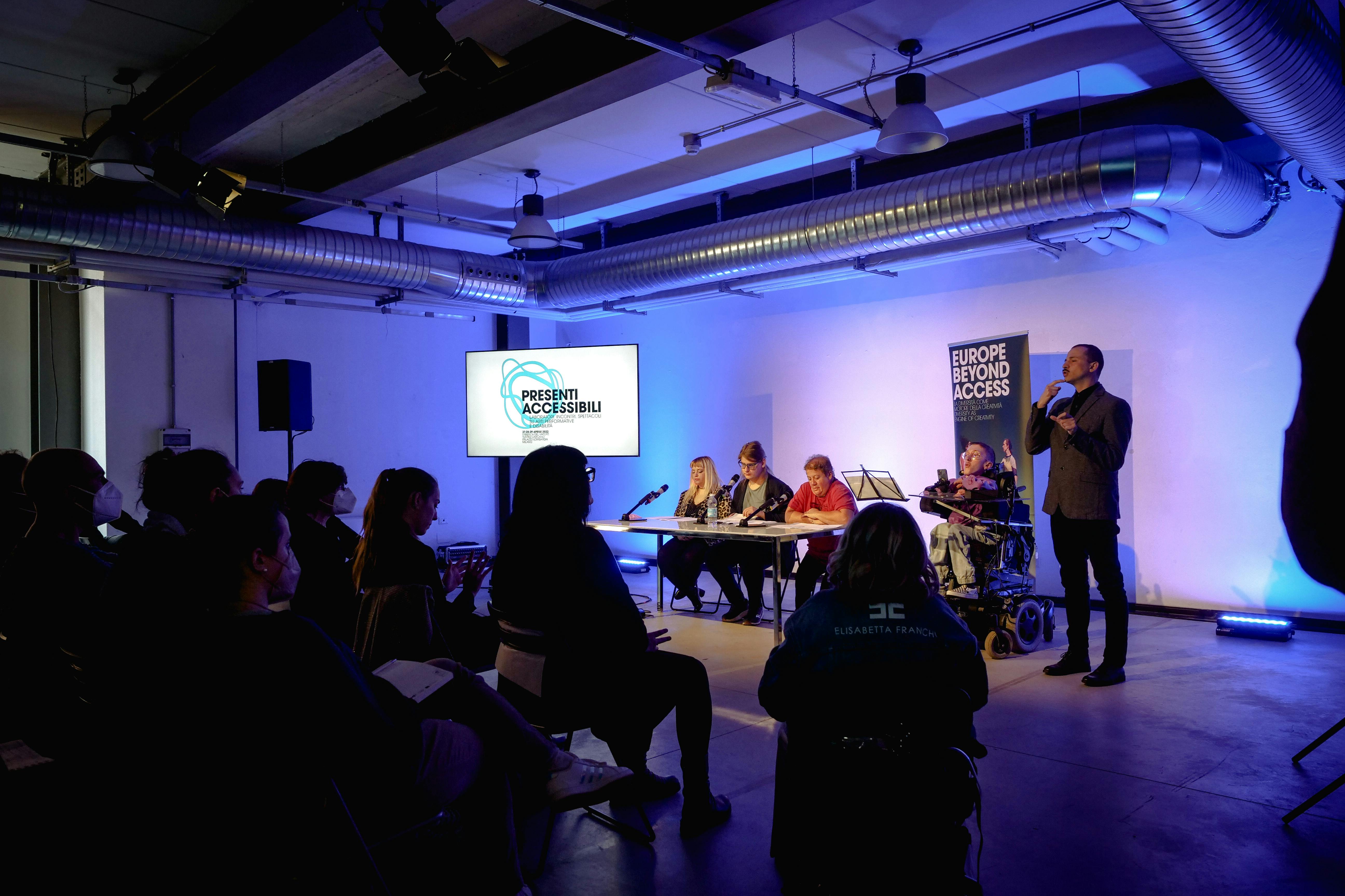 Quattro componenti del gruppo Al.Di.Qua. Artist in una sala conferenze con traduttore LIS