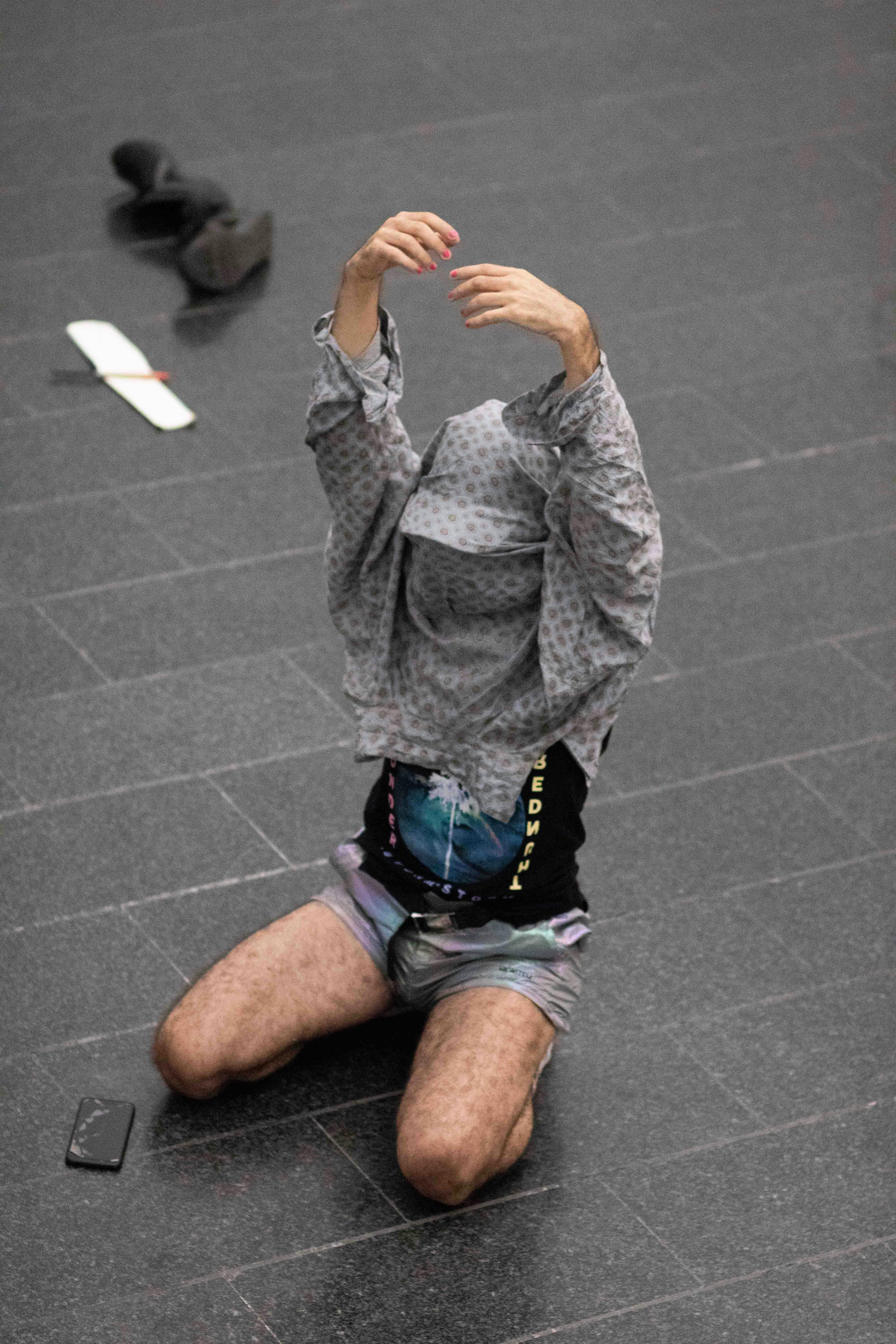 Daniele Ninarello kneeled on the floor; his arms are raised upward. He is wearing a shirt that he lifts to cover his face and head.