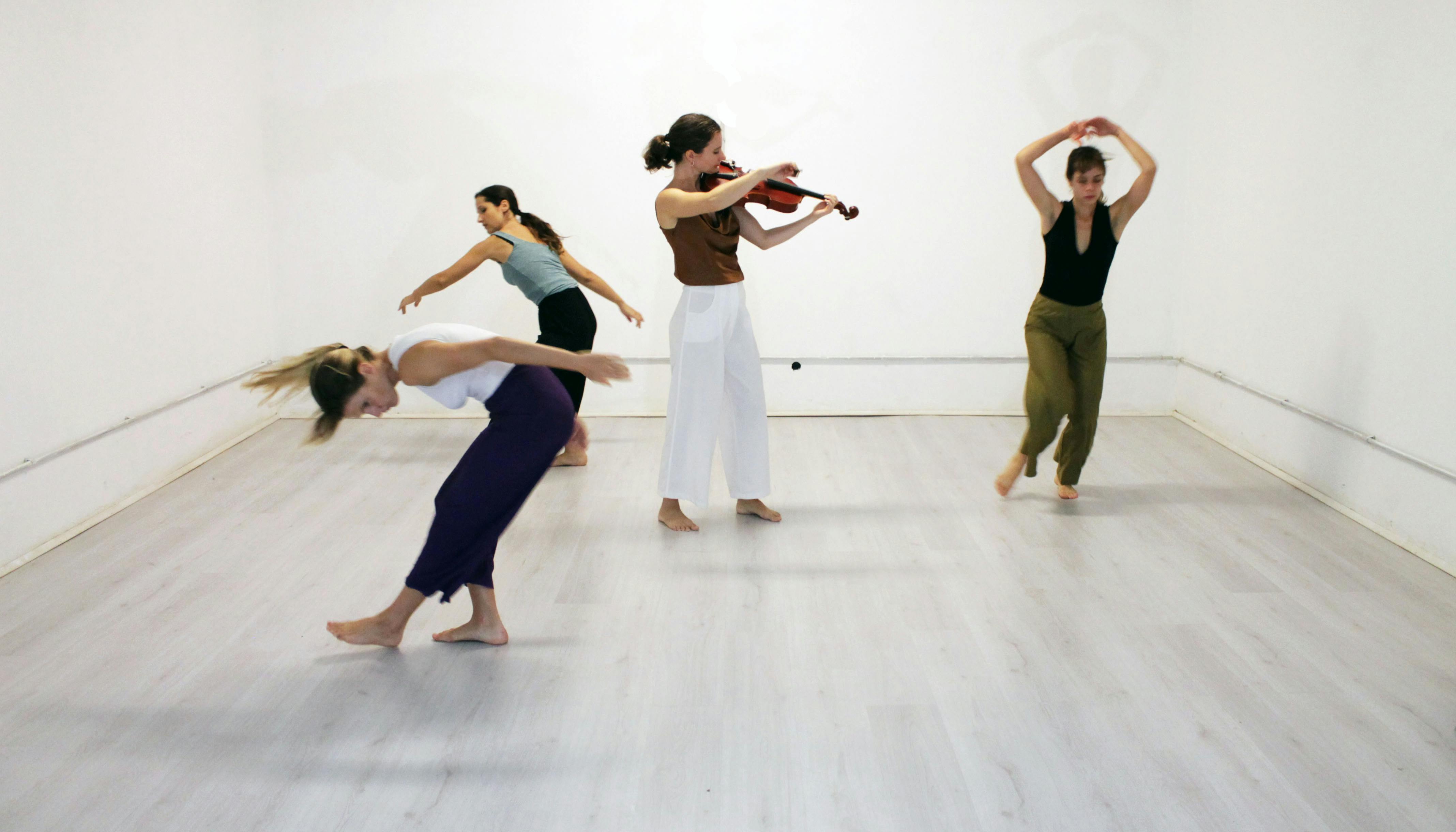 Una violinista al centro della stanza suona e tre interpreti danzano intorno a lei