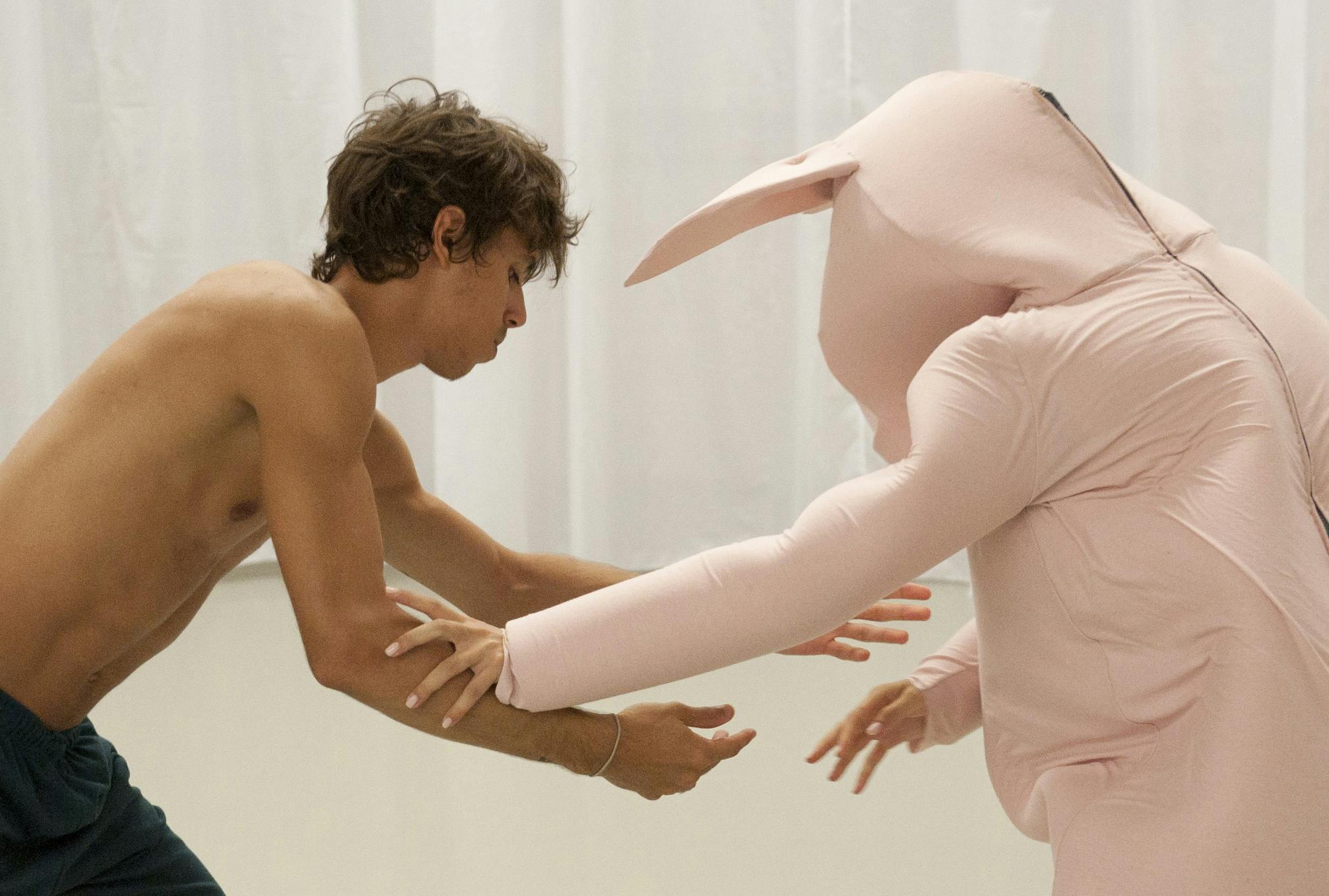 Un danzatore con tuta rosa e uno senza vestito di scena interagiscono 