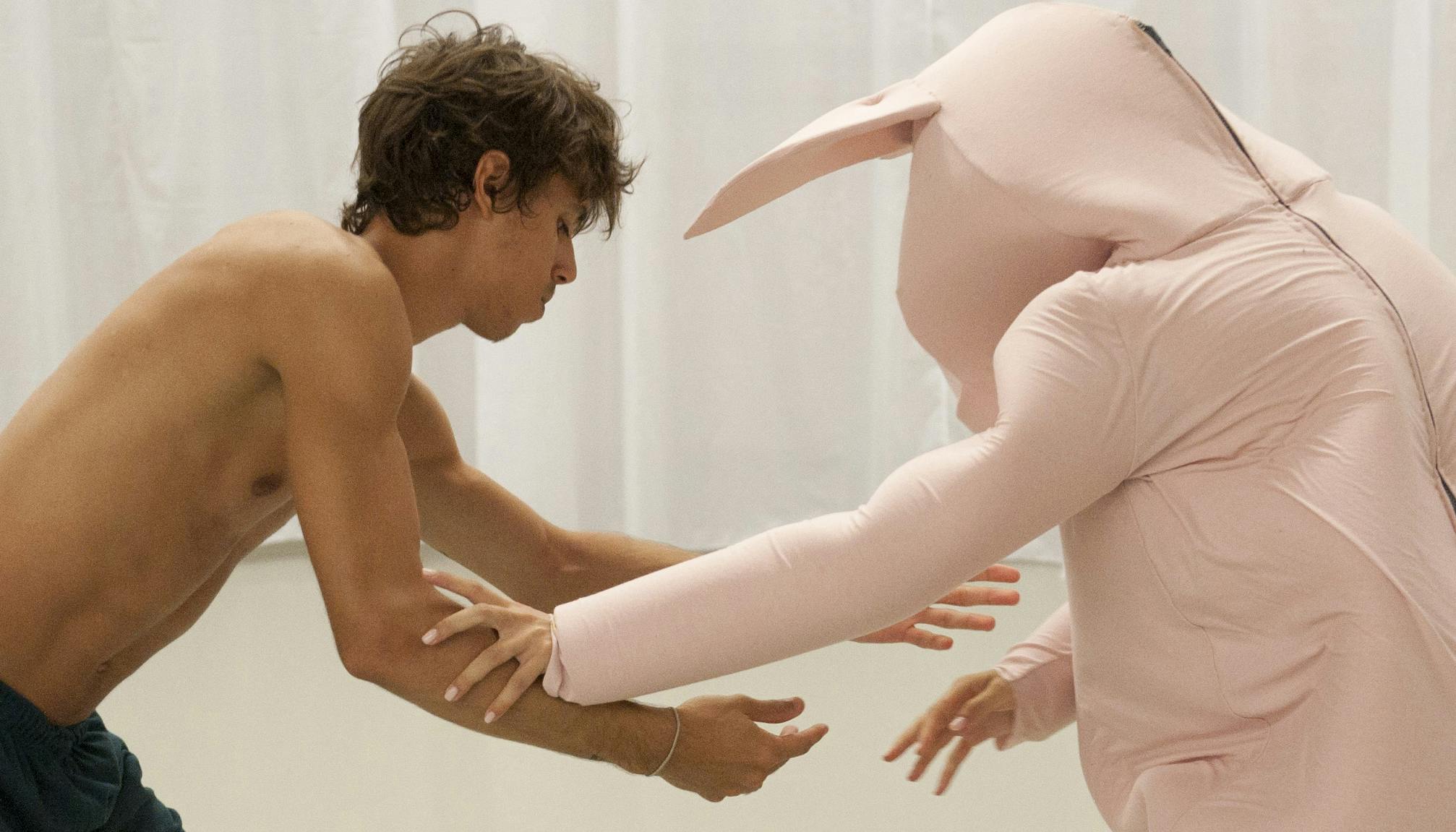 Un danzatore con tuta rosa e uno senza vestito di scena interagiscono 