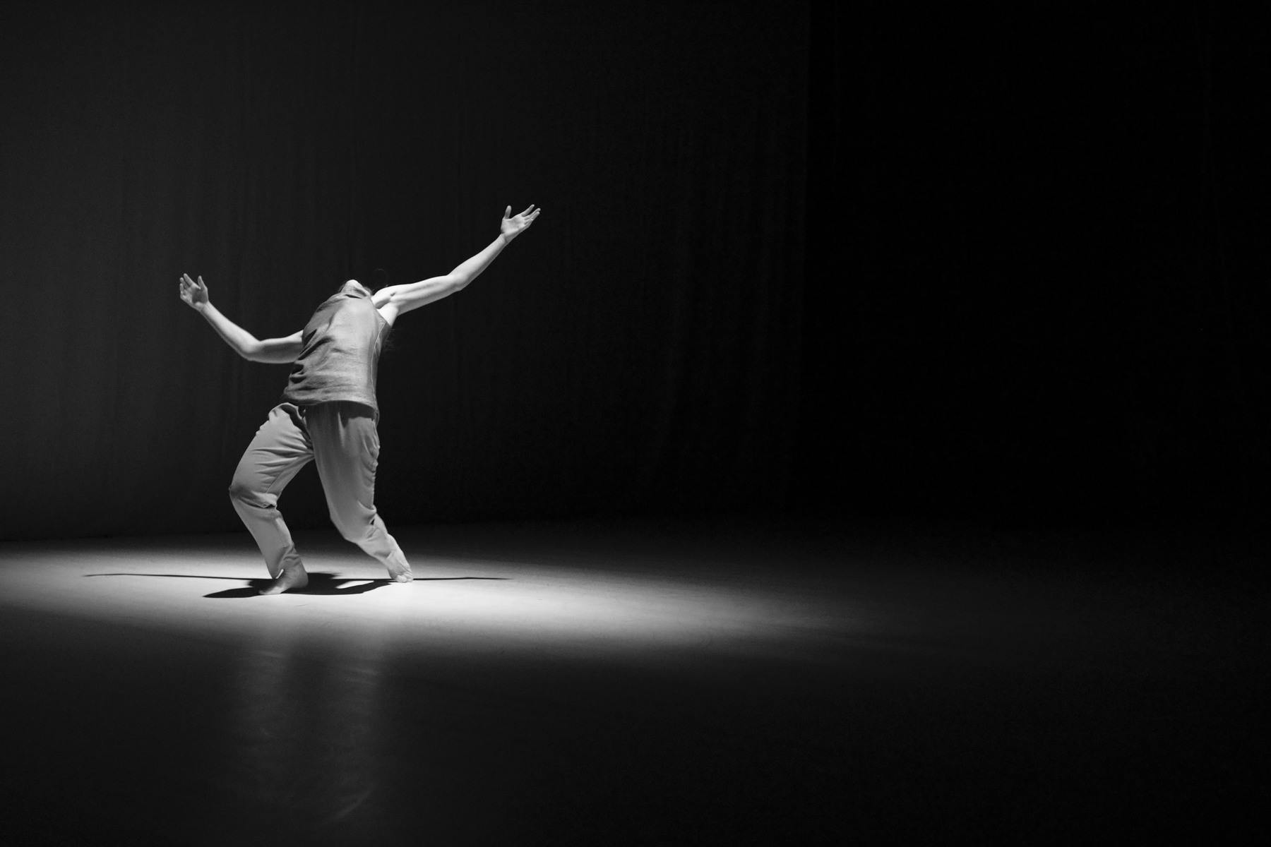 Fotografia in bianco e nero di un performer con una luce ad occhio di bue che si sbilancia indietro guardando in alto 