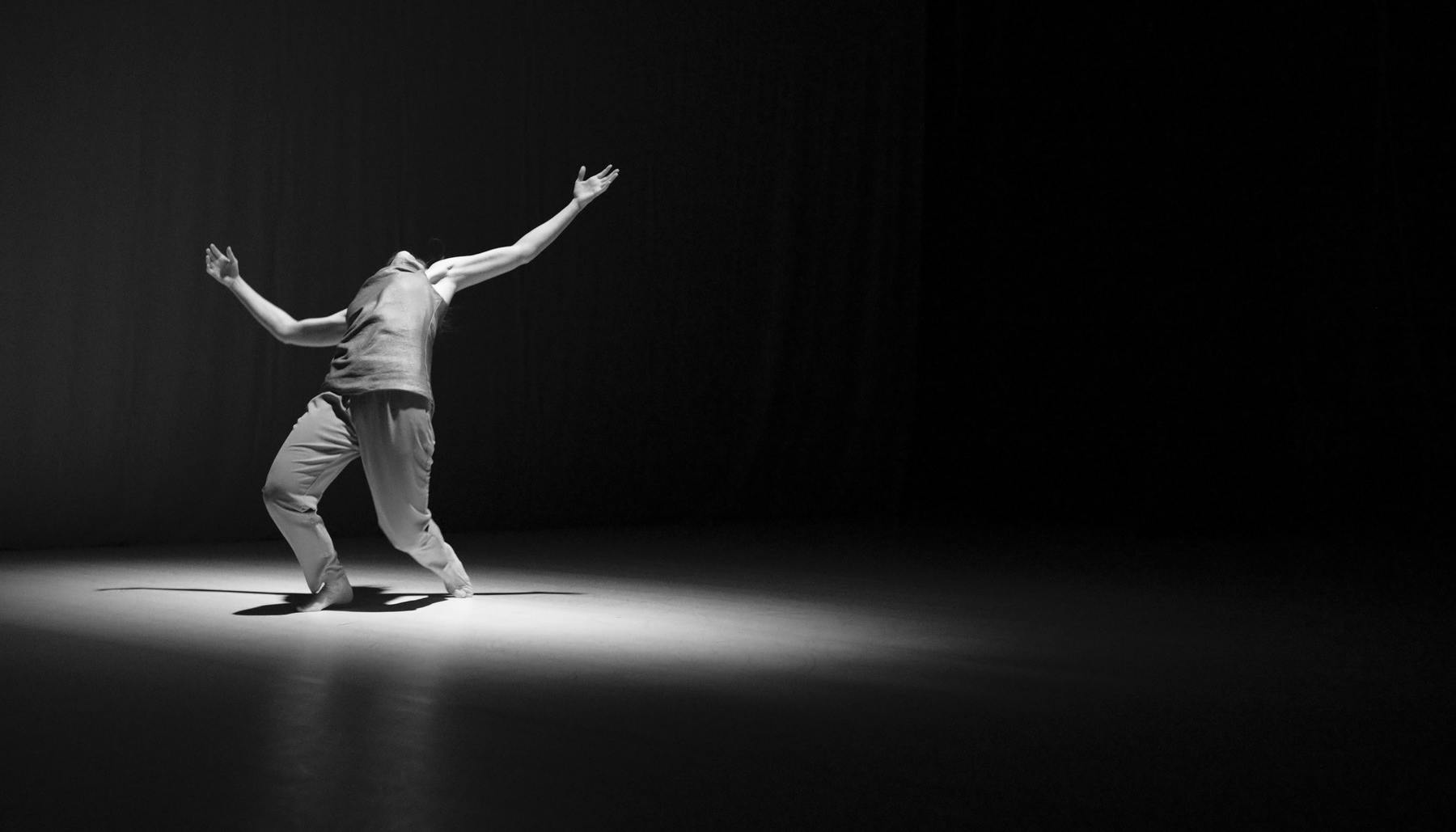 Fotografia in bianco e nero di un performer con una luce ad occhio di bue che si sbilancia indietro guardando in alto 